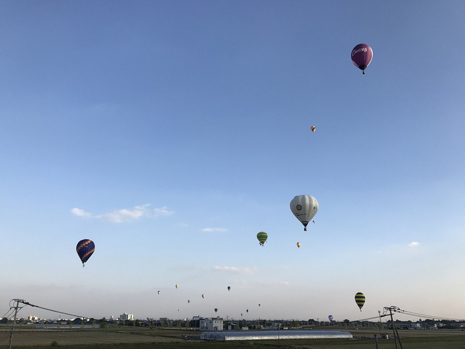 A colorful hot air balloon drifting above green fields at sunrise, its envelope glowing in the early light.