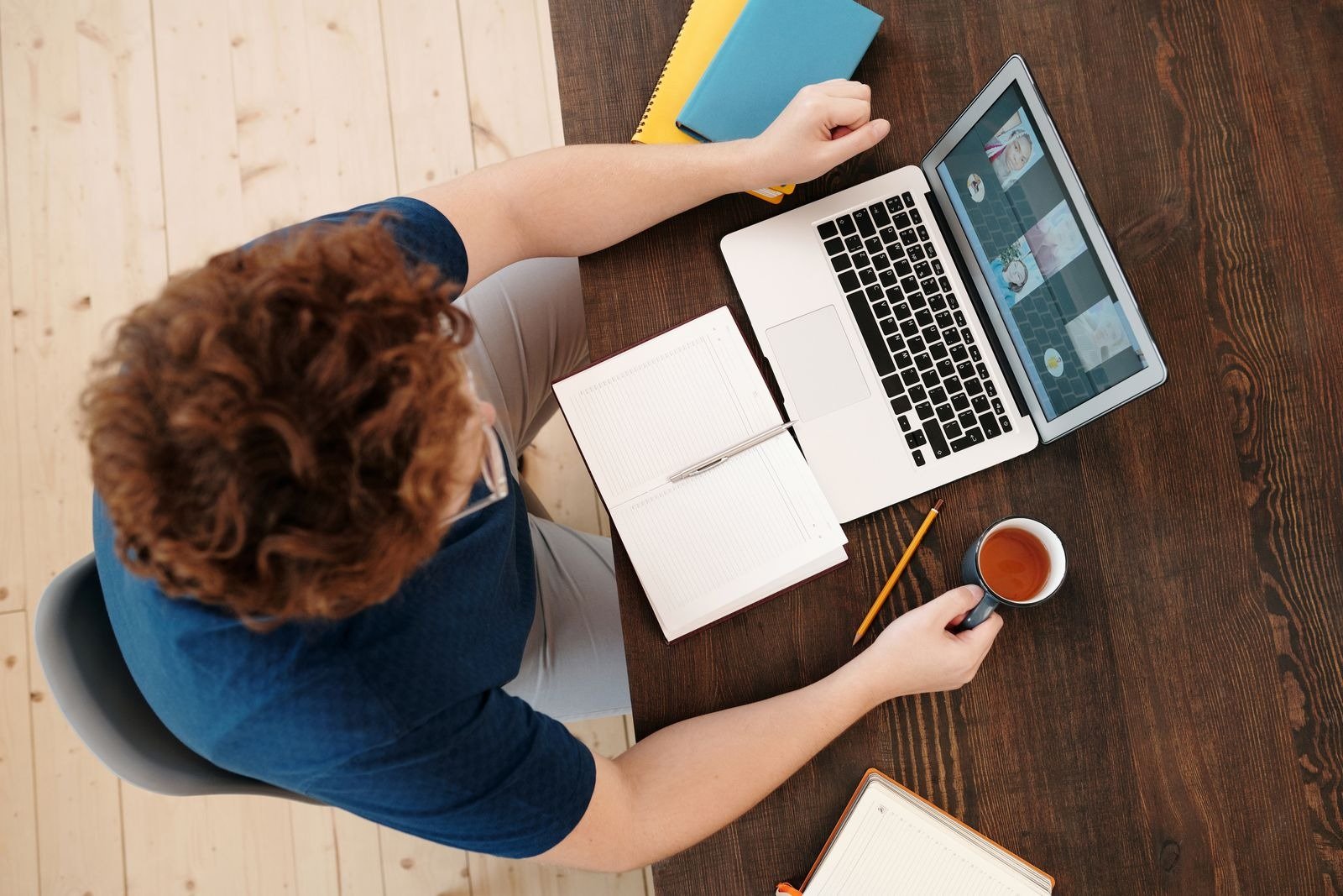 A top-down view of a person on a video call on a laptop, with a notebook, pencil, and cup of tea.