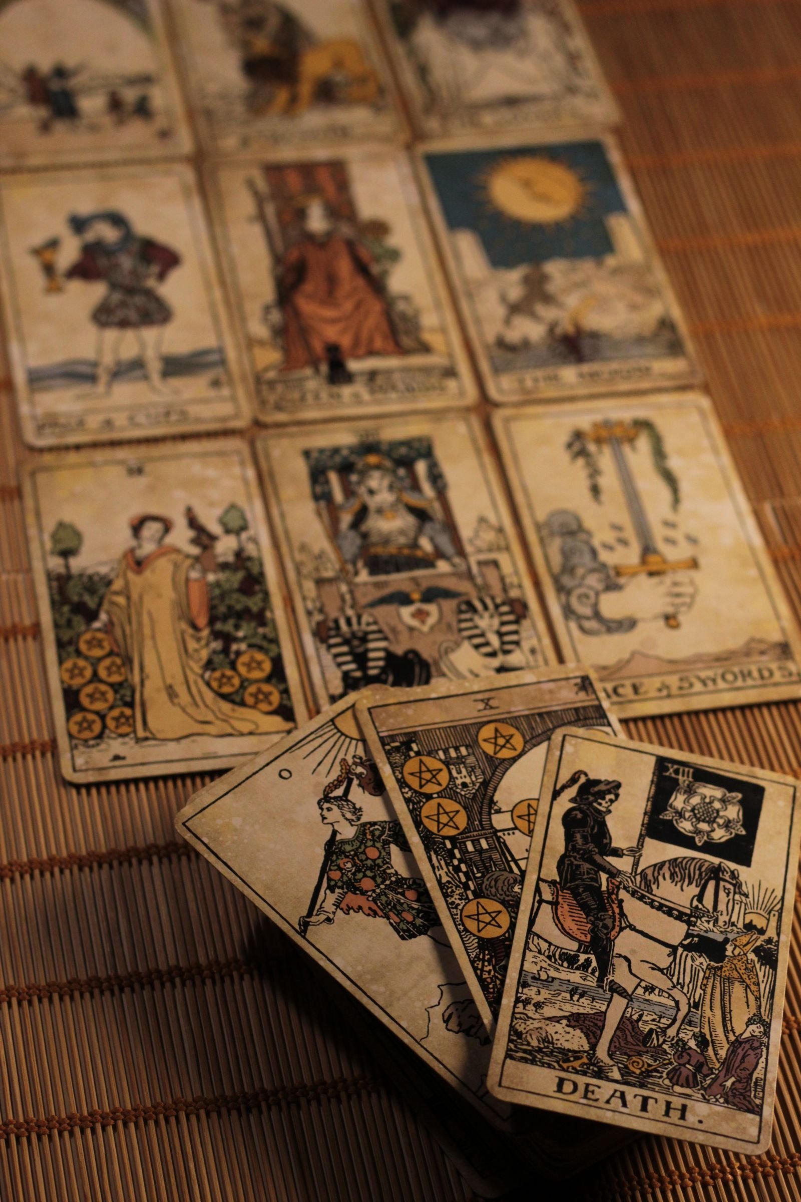Vintage-style tarot cards arranged on a bamboo mat, including Death, the Ten of Pentacles, and the Ace of Swords.