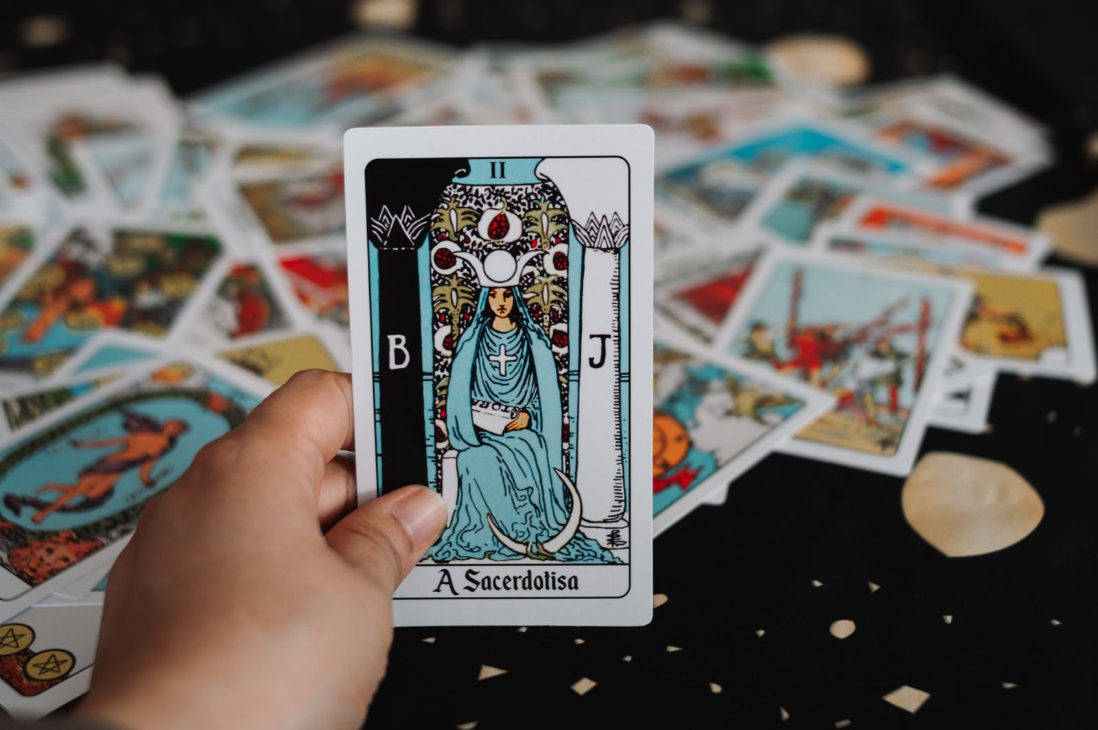 A hand holding The High Priestess tarot card (titled A Sacerdotisa) upright over a scattered deck.