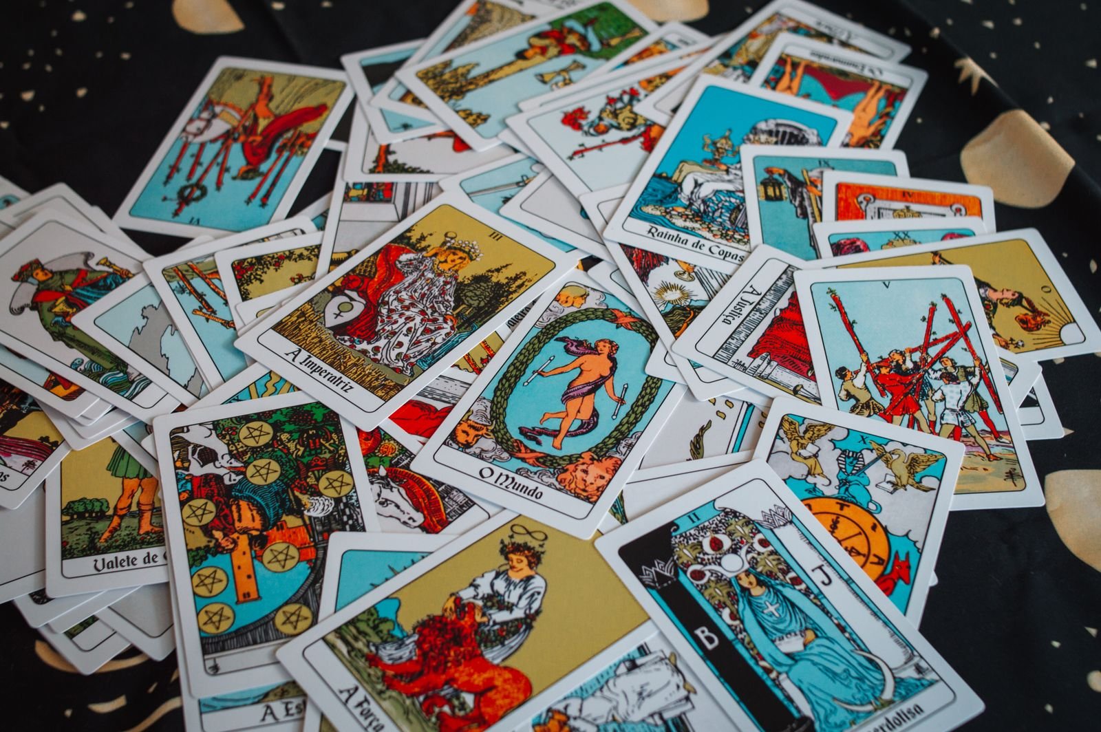 A wide scatter of colorful Rider-Waite-style tarot cards with Portuguese titles, including The Empress, The World, and Strength, on a black star-patterned cloth.