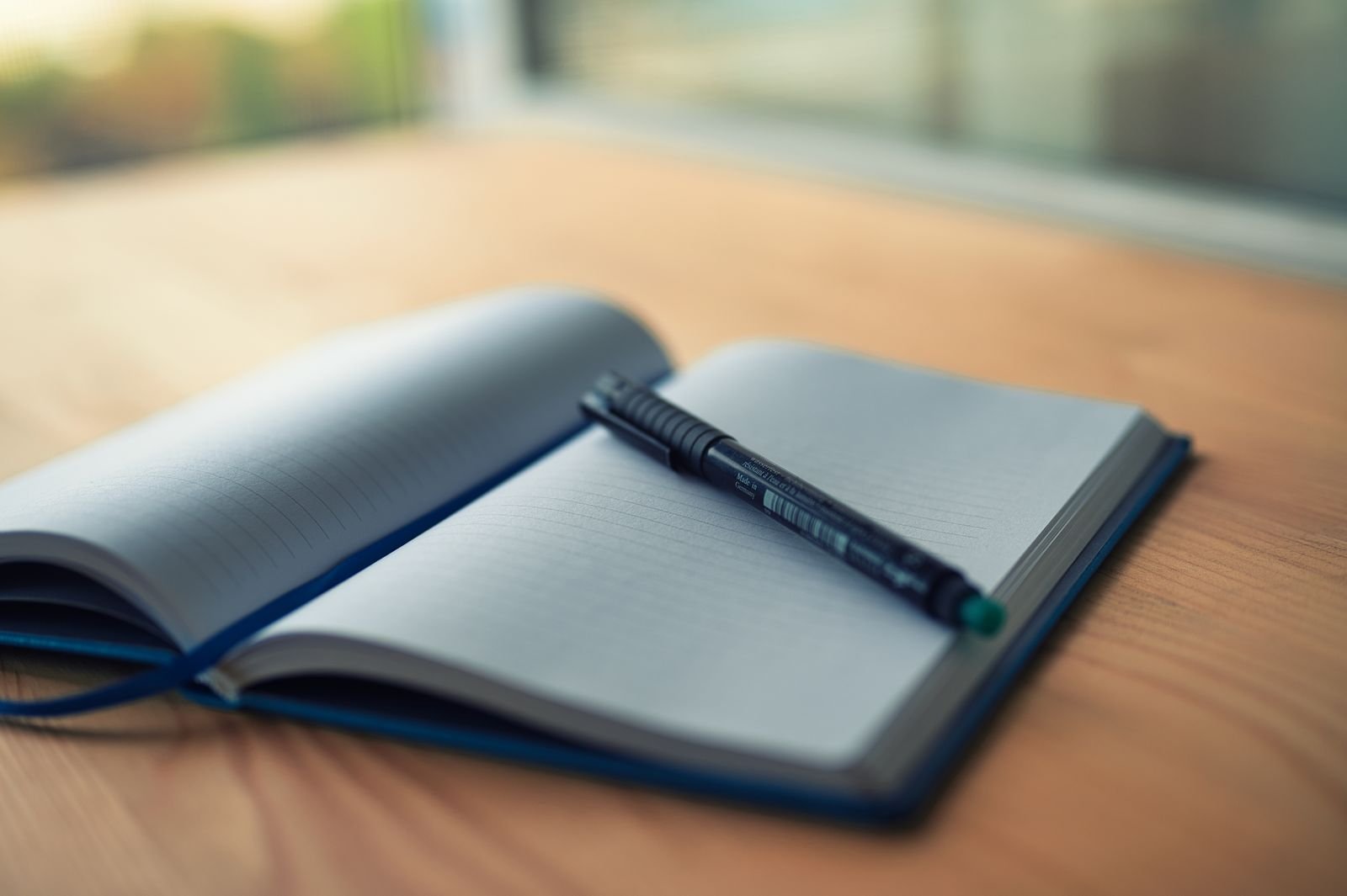 An open lined notebook with a pen resting on a wooden desk