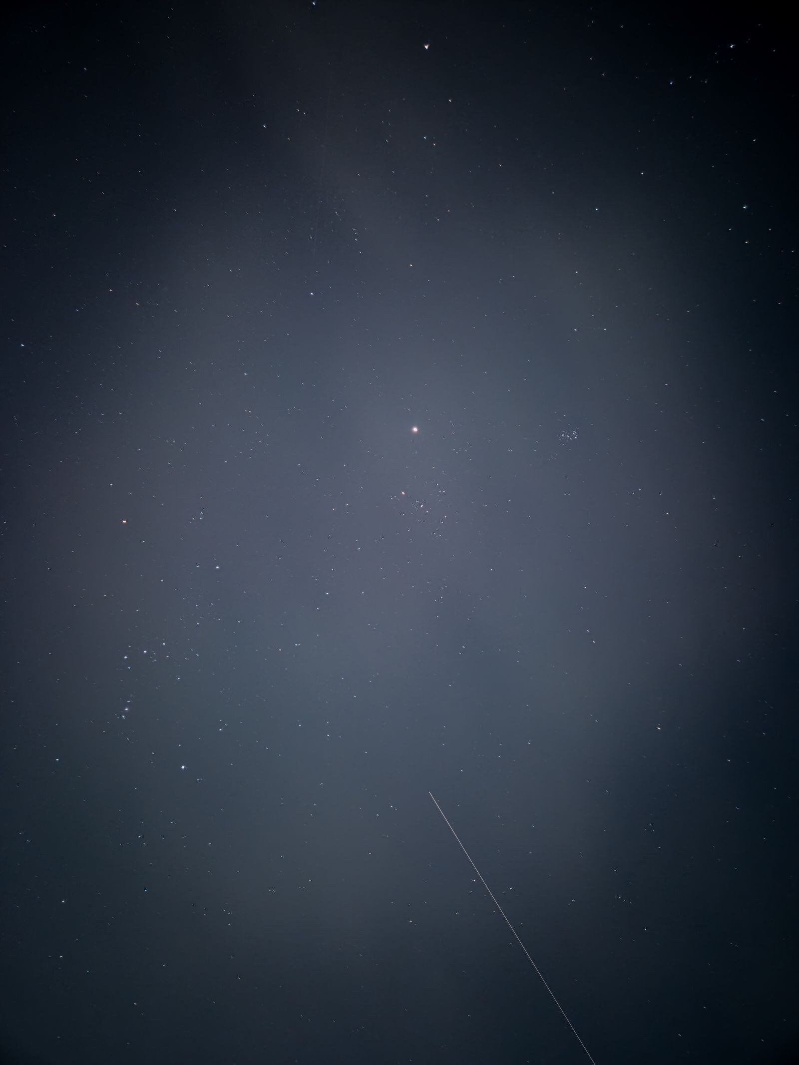Starry night sky with a bright star and a thin satellite trail crossing the darkness.
