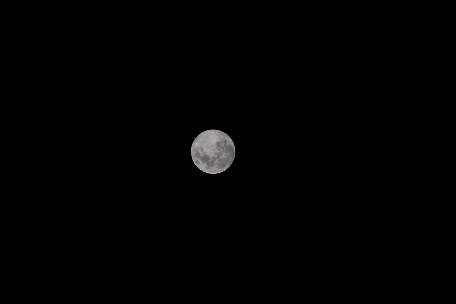 A close-up photograph of the full moon's disc against a black sky, showing its dark plains.