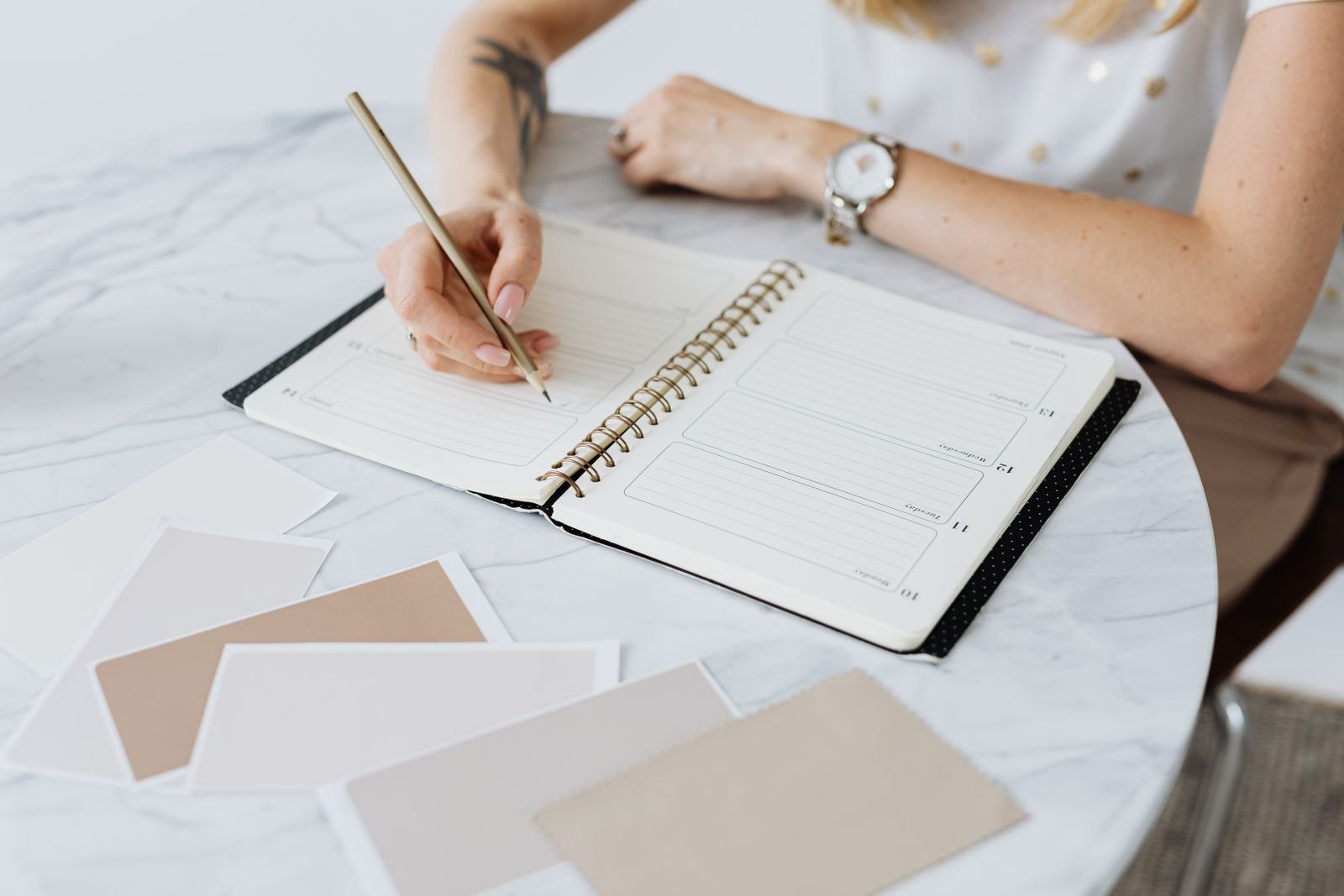 A woman writing in a spiral-bound weekly planner on a marble table.