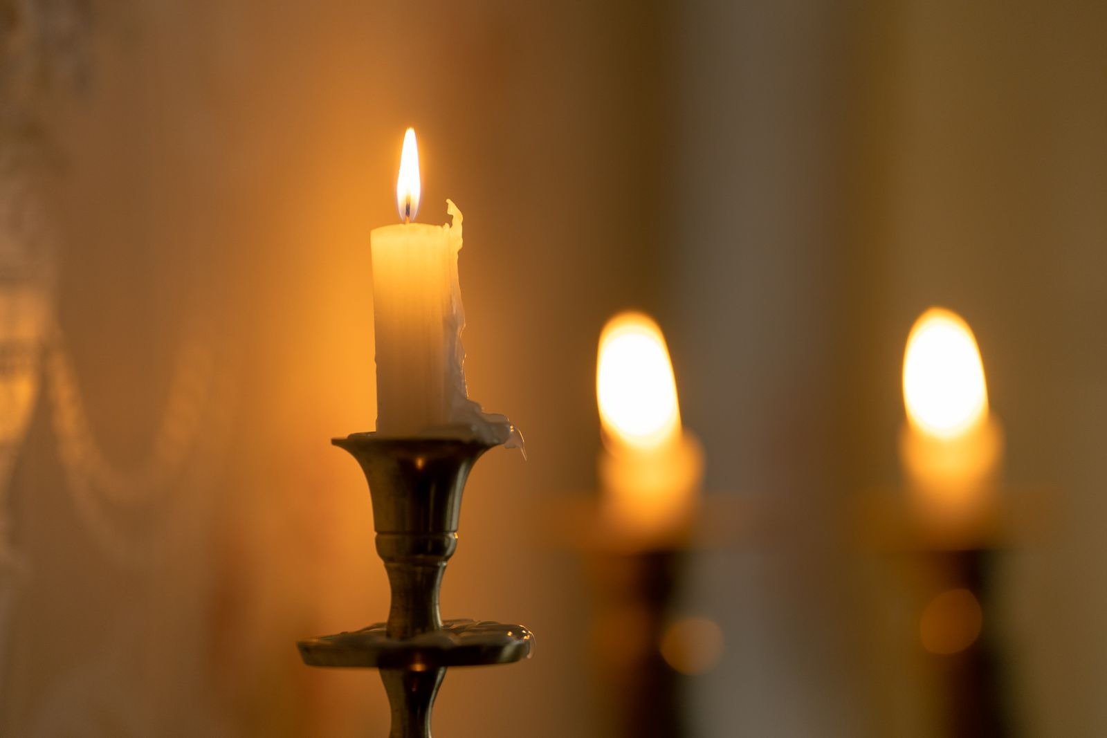 A lit candle in a brass holder with two more candles glowing softly behind it.