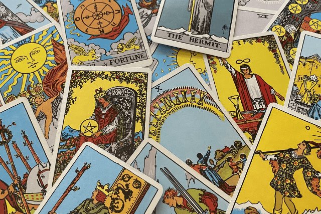 Rider-Waite tarot cards scattered and overlapping, showing the Wheel of Fortune, the Hermit, and the Magician.
