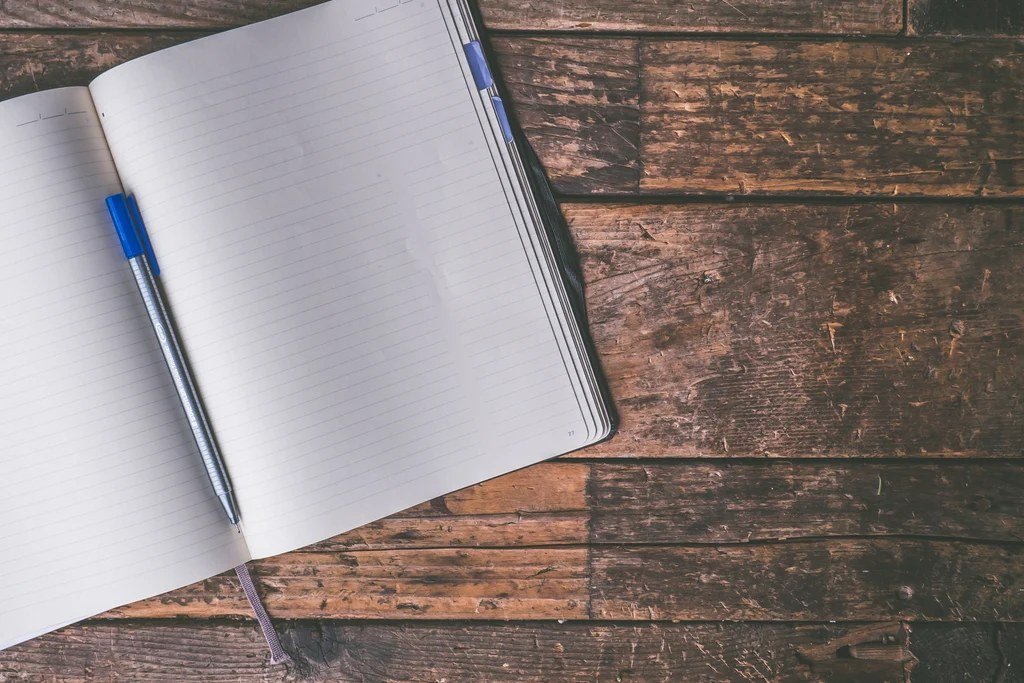 Open blank journal with a blue pen on a rustic wooden table