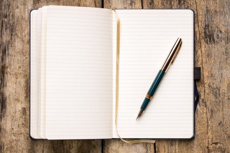 Open blank notebook with a teal and gold pen on a wooden table
