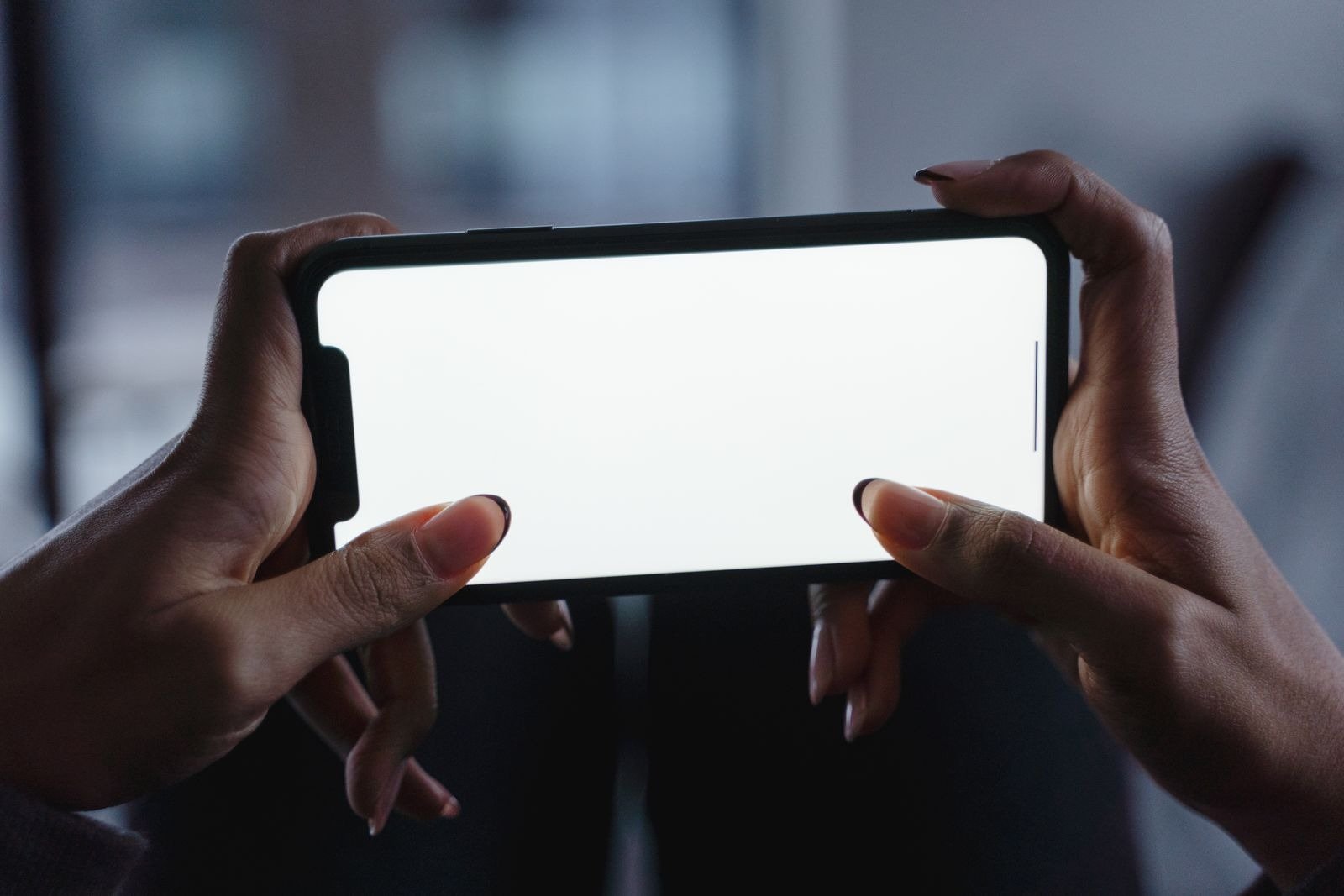 Two hands holding a smartphone horizontally with a blank white screen.