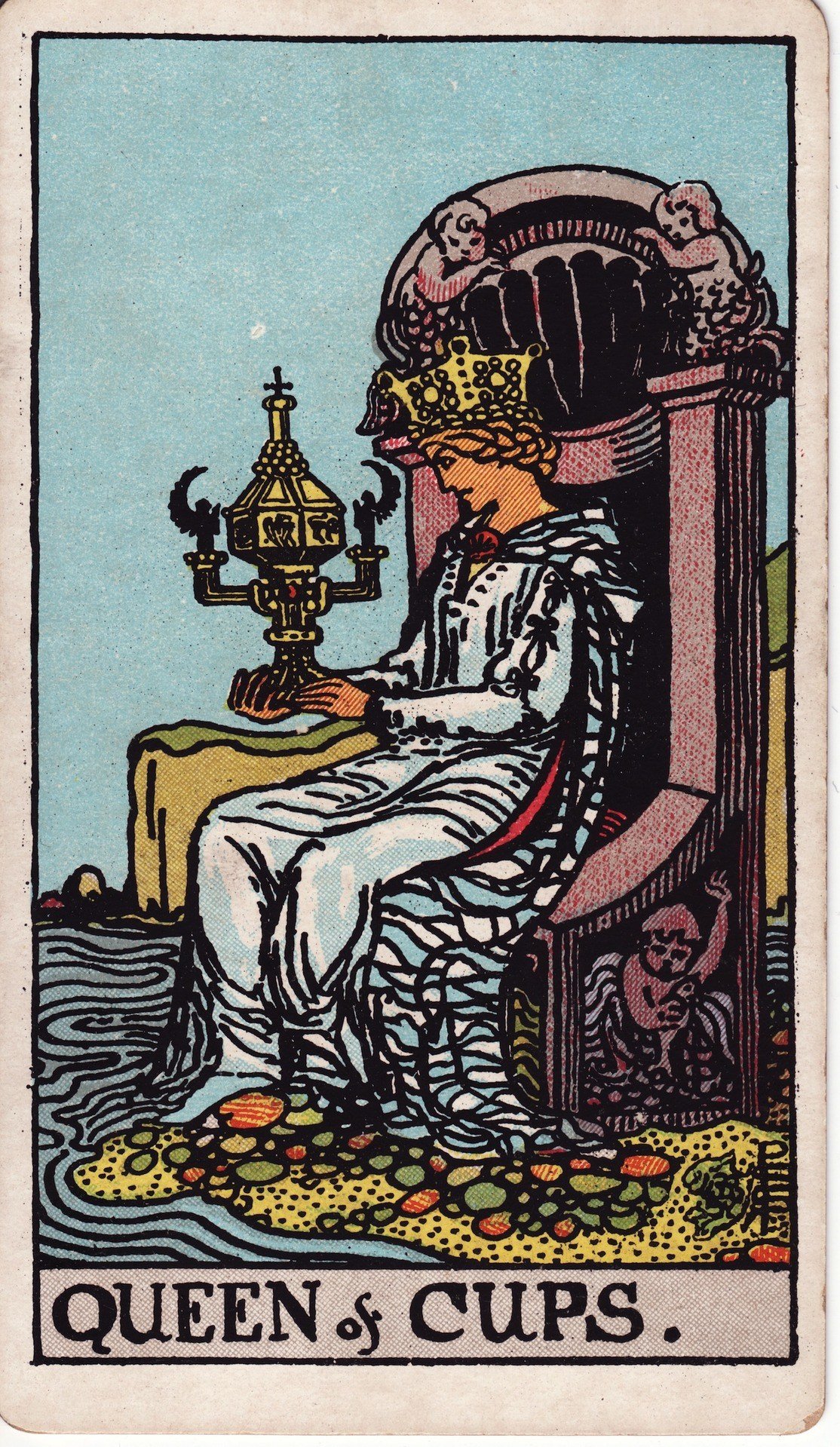 The Queen of Cups from the Rider-Waite-Smith tarot deck: a serene queen sits on a stone throne at the water's edge, gazing into an ornate covered cup she holds with both hands.