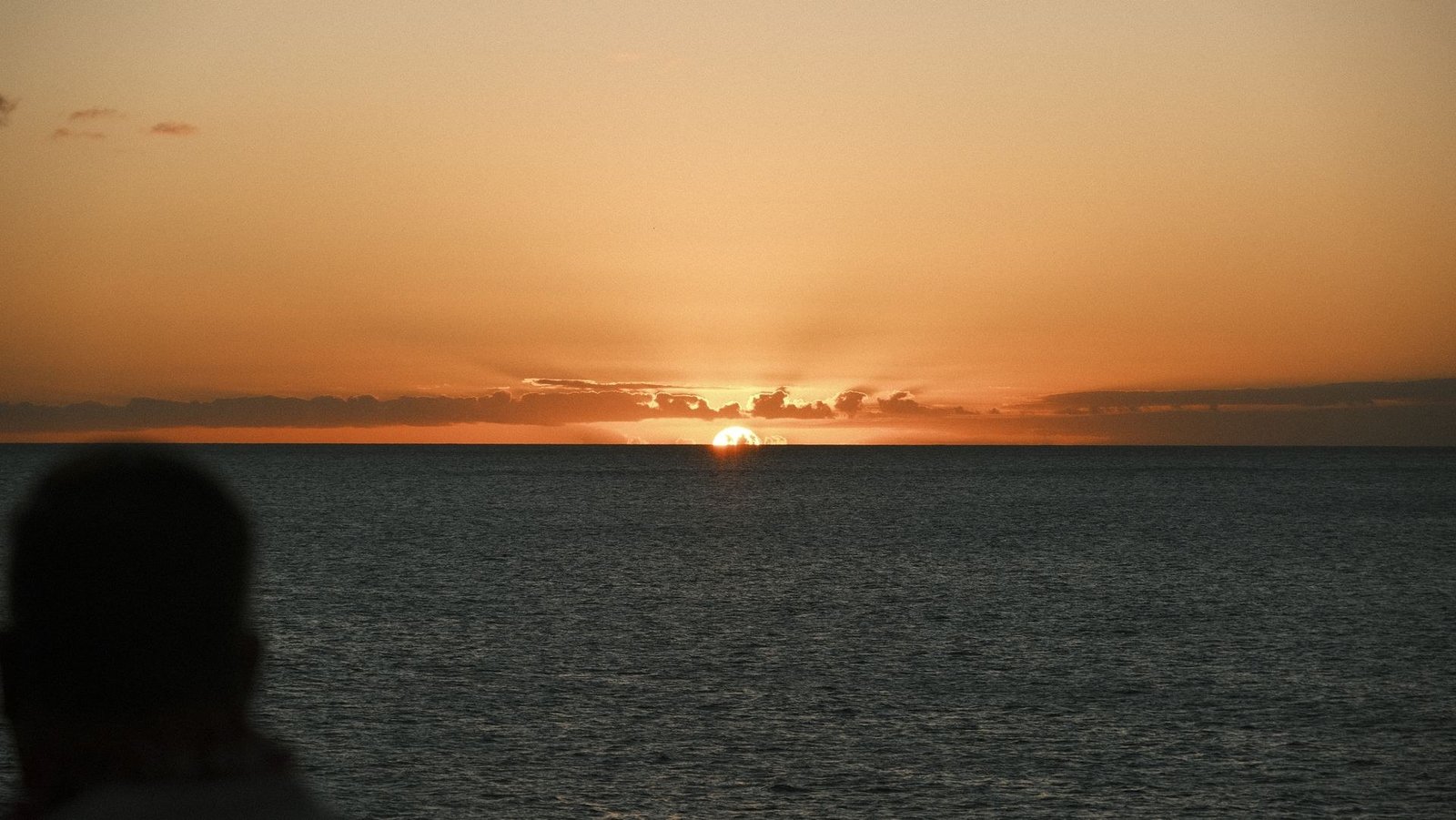 Silhouette of a person watching the sun set over the ocean.
