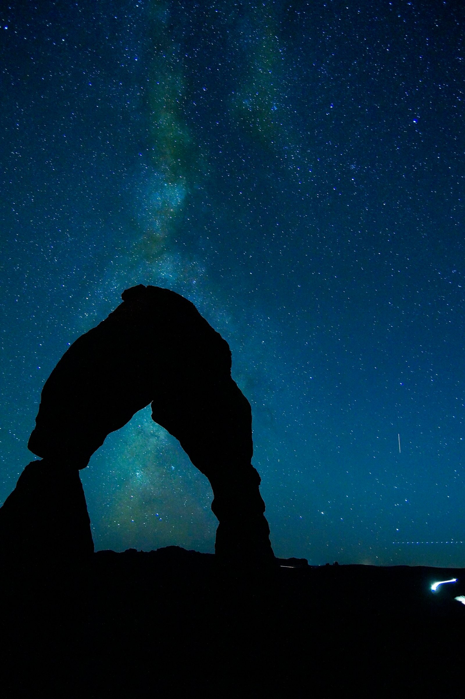 A dark natural rock arch silhouetted against a star-filled sky with the faint Milky Way.
