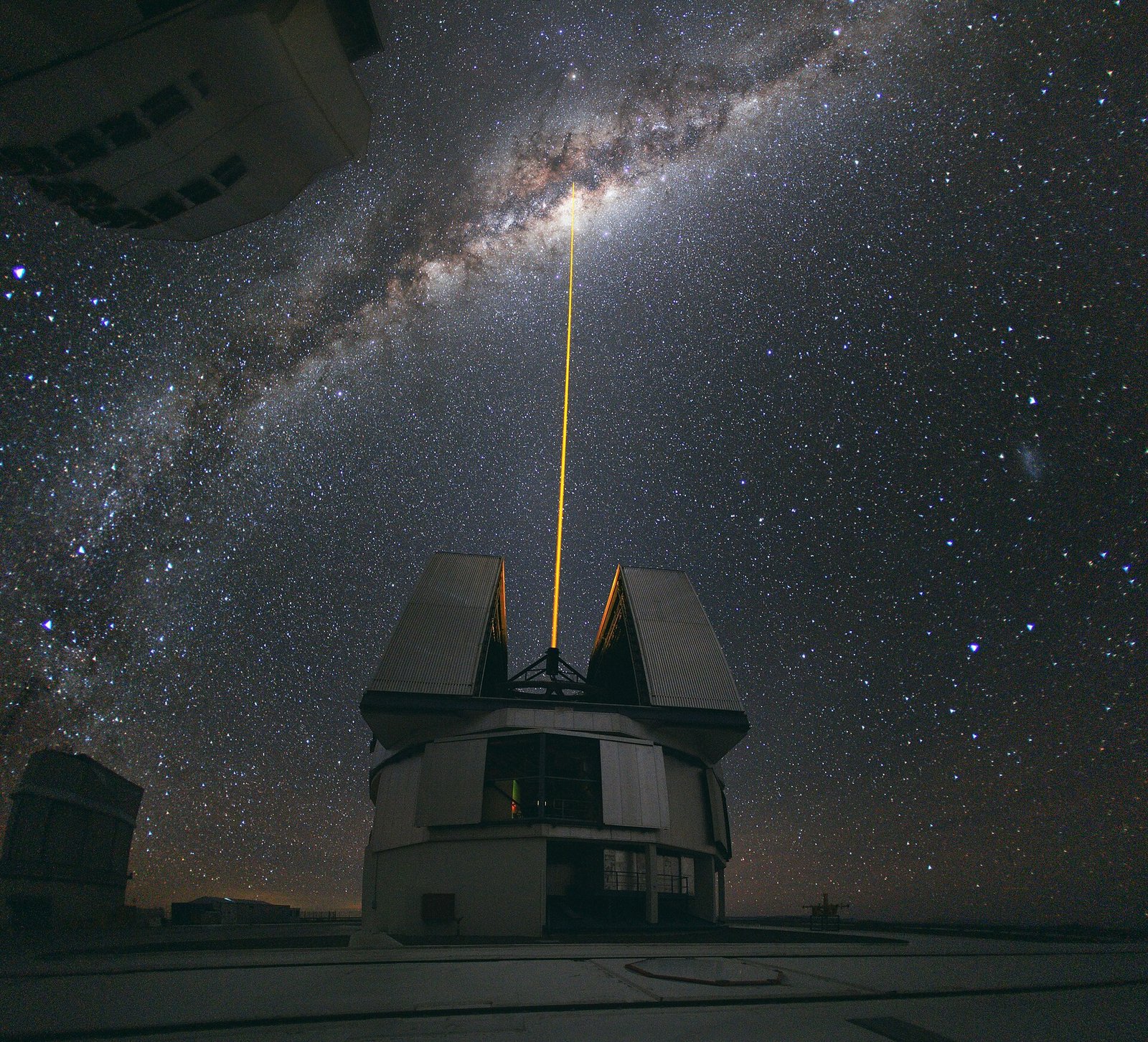 An observatory telescope firing a yellow laser guide-star beam into the Milky Way on a starry night.