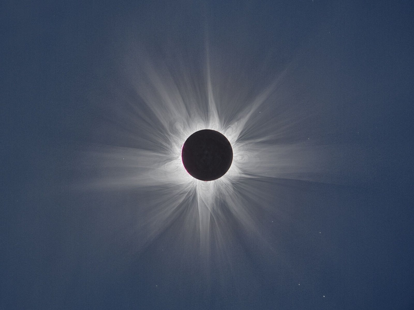 Total solar eclipse corona with fine white streamers radiating into a dark blue sky