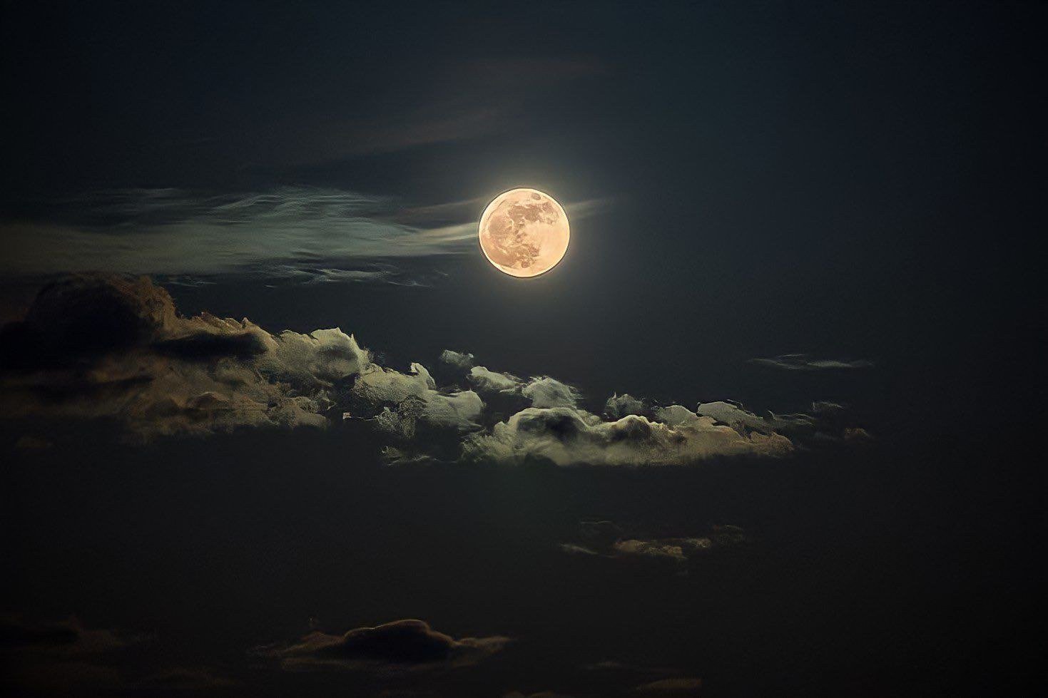 Full moon glowing above a bank of clouds in the night sky
