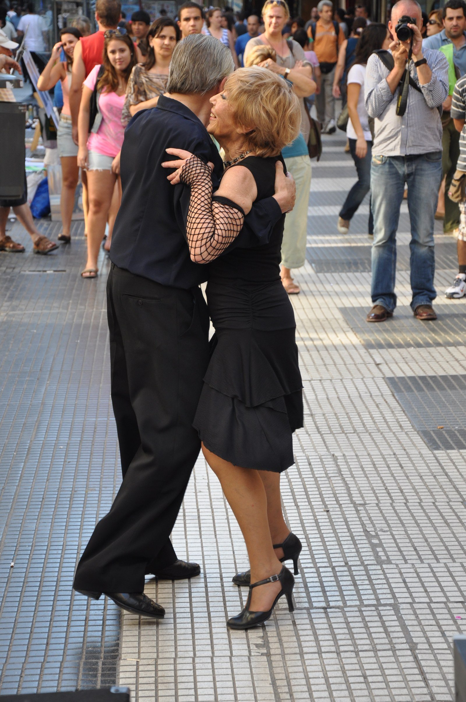 An older couple dancing tango on a busy pedestrian street while onlookers watch