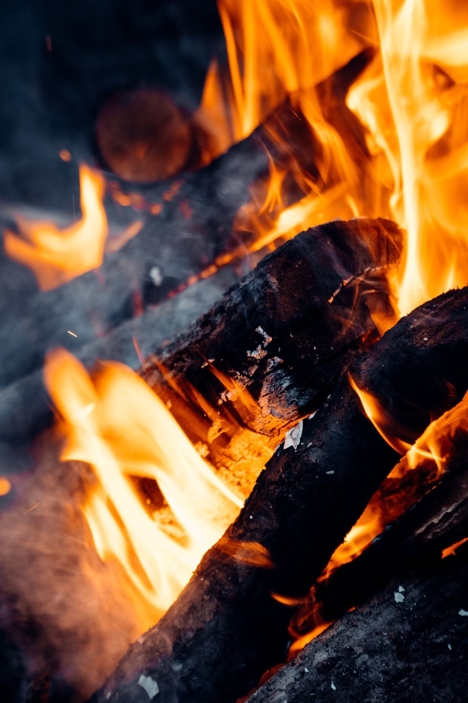 Close-up of bright orange flames curling upward from burning logs, glowing embers visible at the base.