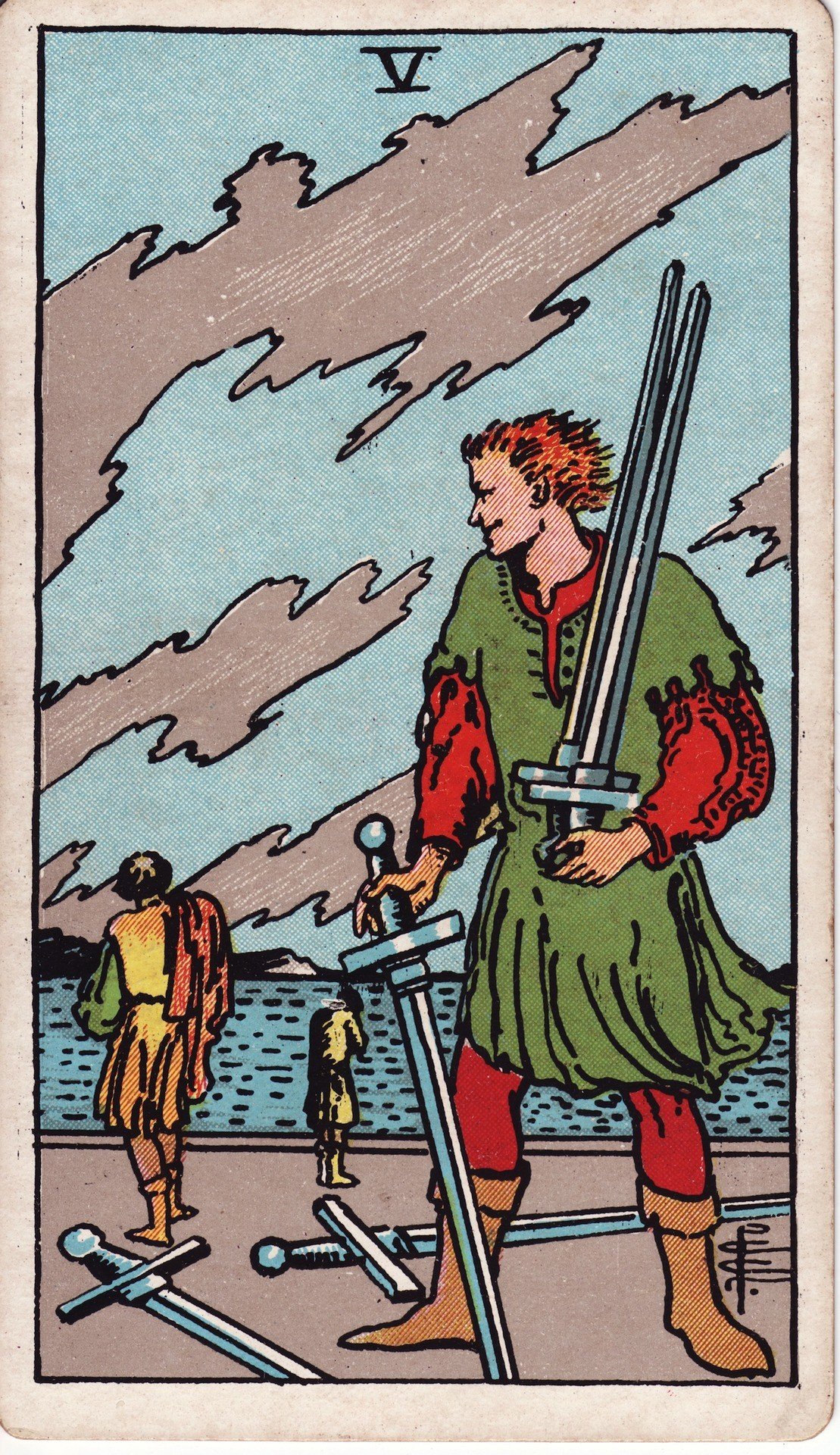 The Five of Swords from the Rider-Waite-Smith tarot deck: a smirking man holds three swords while two defeated figures walk away toward a gray sea, two more swords lying on the ground.