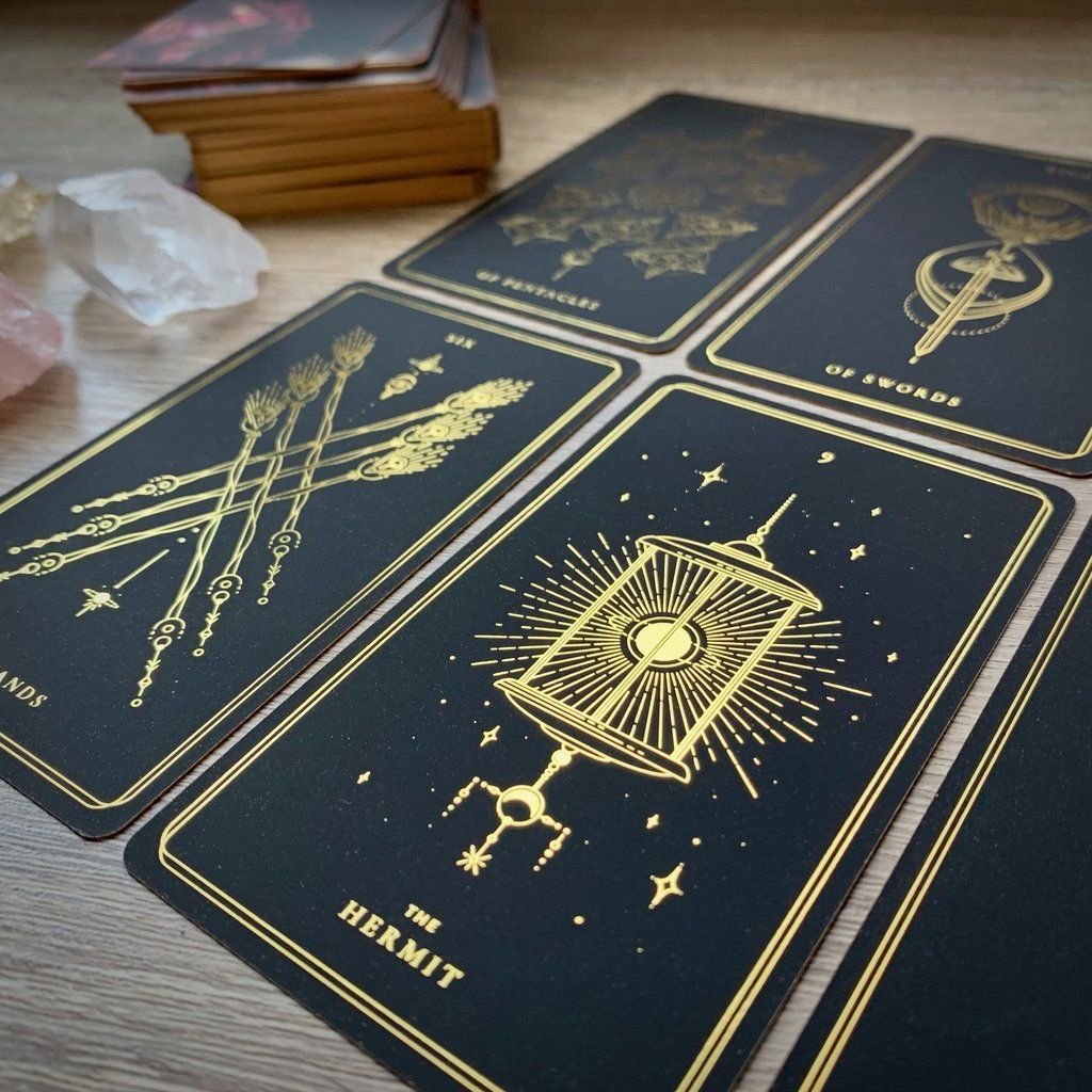 Black-and-gold tarot cards including The Hermit laid out on a wooden table beside a crystal