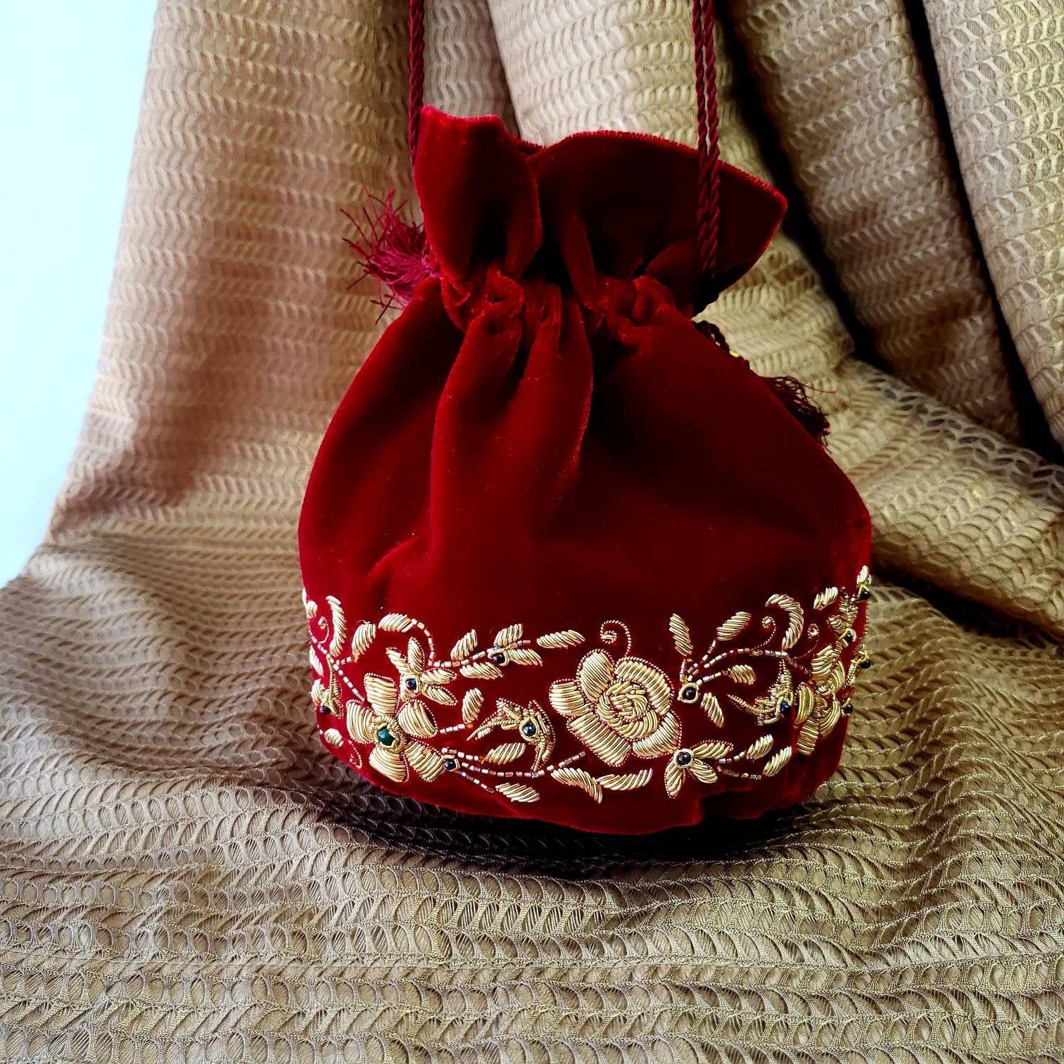 A deep red velvet drawstring pouch with gold floral embroidery.