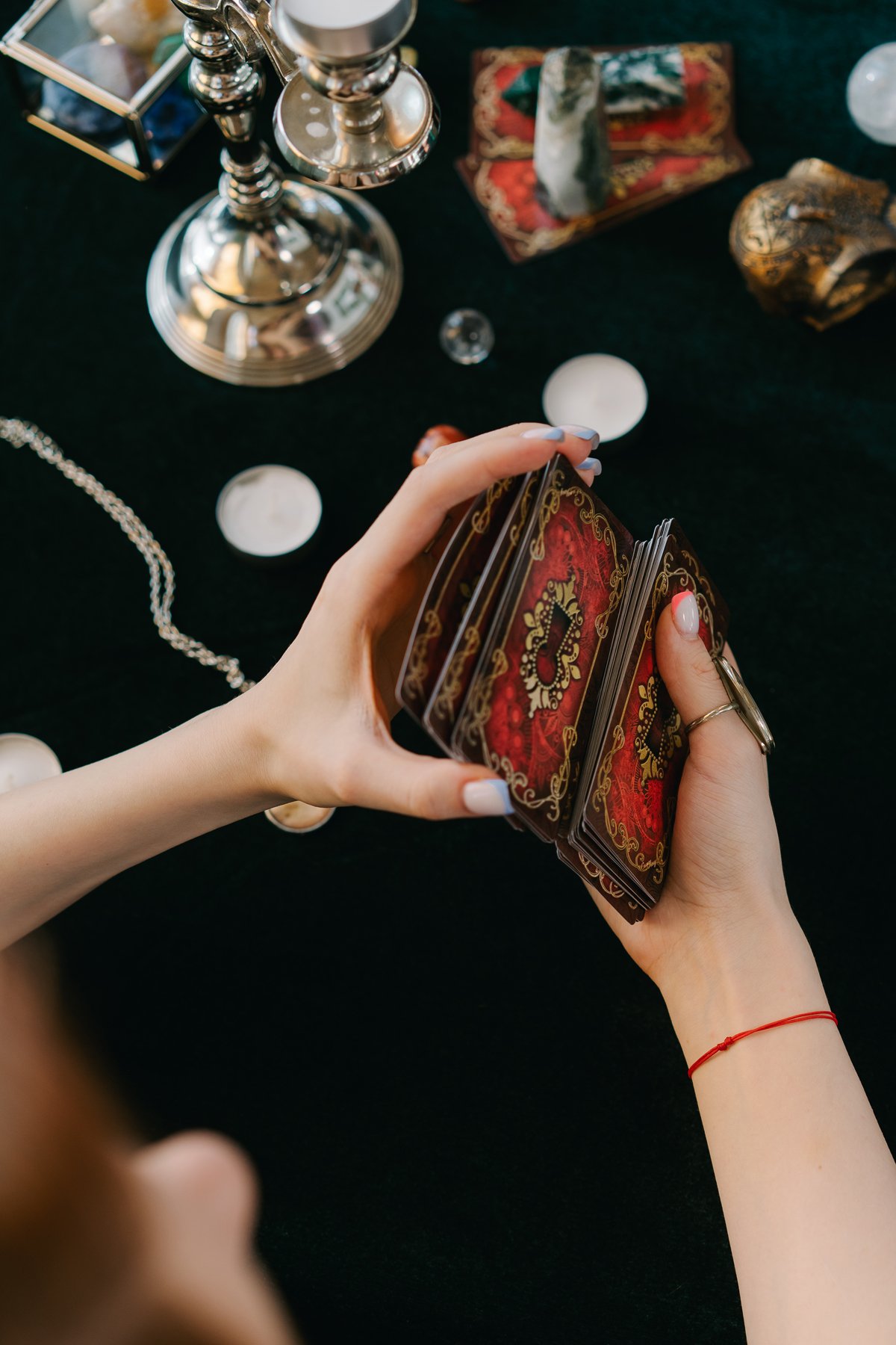 Hands holding tarot cards over a dark table with candles and crystals