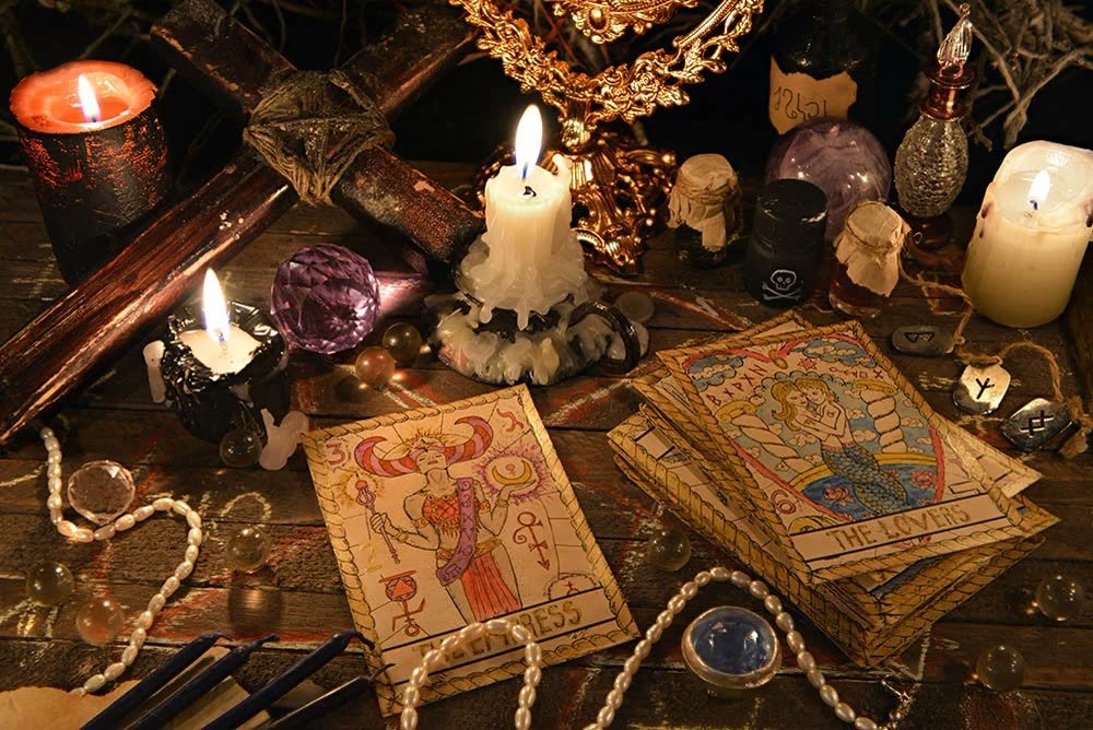 Tarot cards, lit candles, a crystal ball, and beads arranged on a wooden table