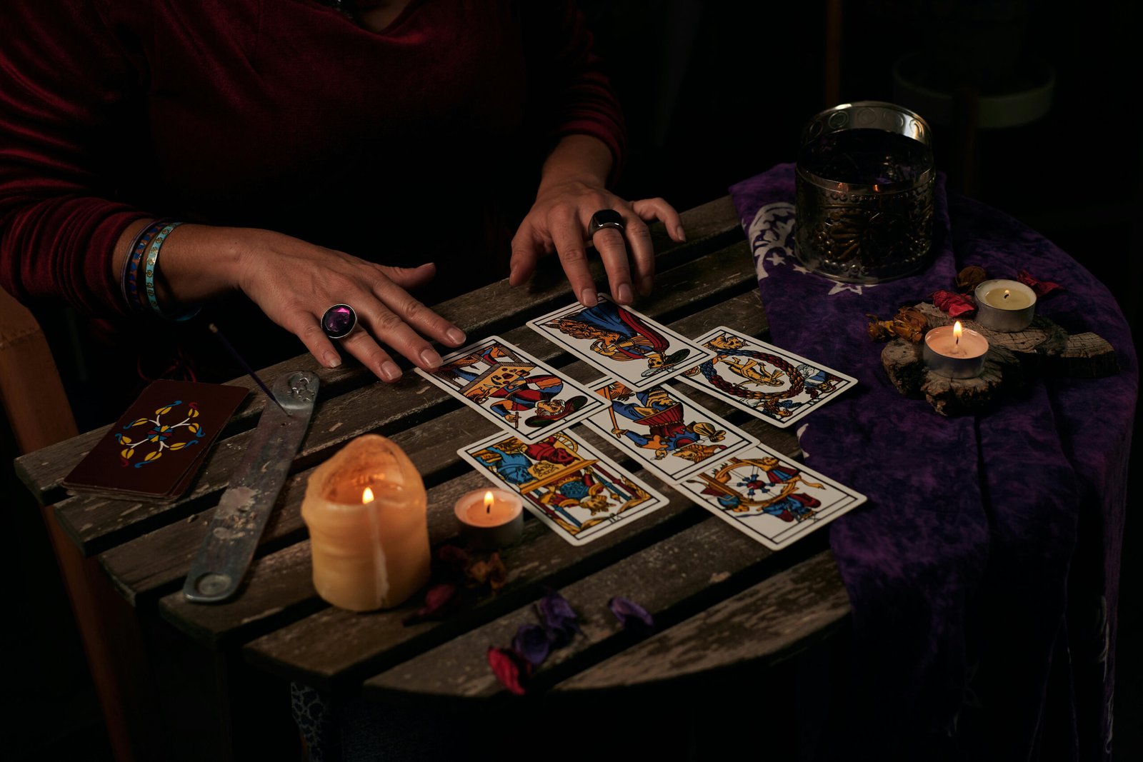 Hands arranging tarot cards on a small wooden table lit by candles