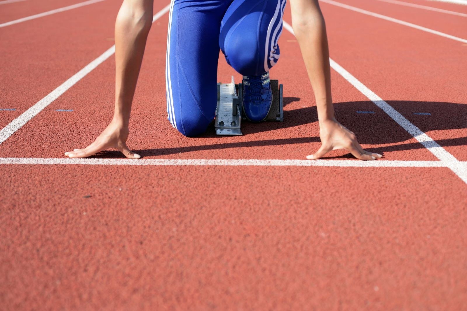 An athlete crouched in starting blocks on a red running track, hands on the ground, poised for the start.