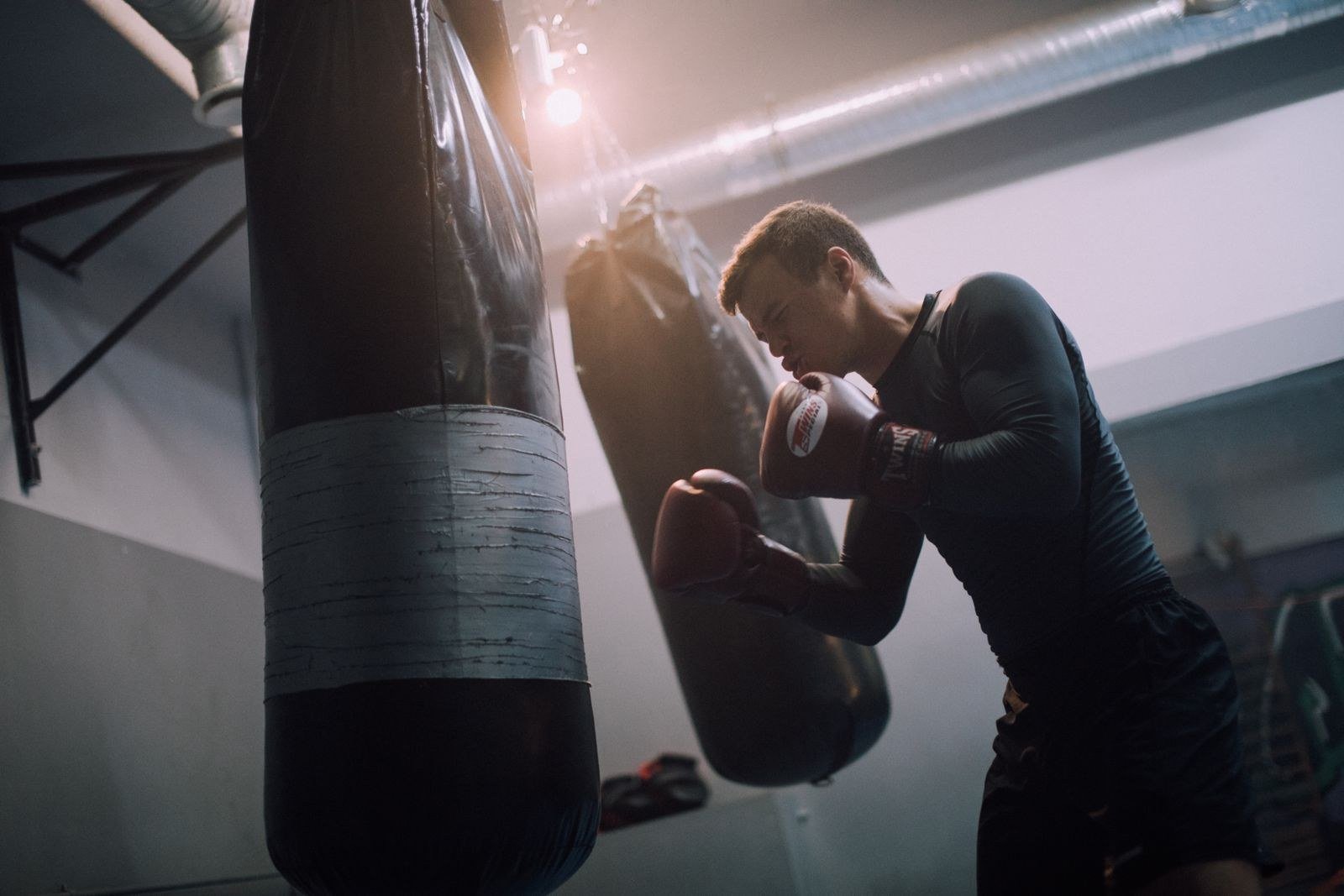 A boxer in gloves facing a heavy punching bag in a gym, in a guard stance.