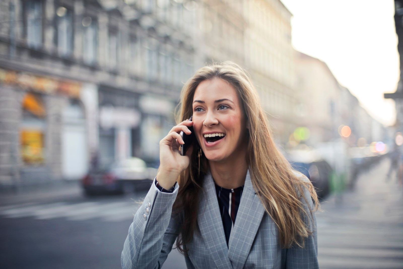 A young woman talking on a smartphone while walking down a bright city street, mid-conversation with an expressive gesture.
