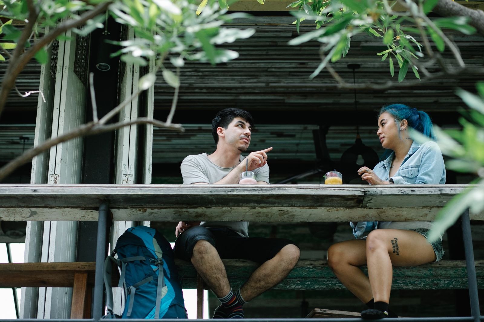 Two young people talking over drinks at an outdoor cafe table.