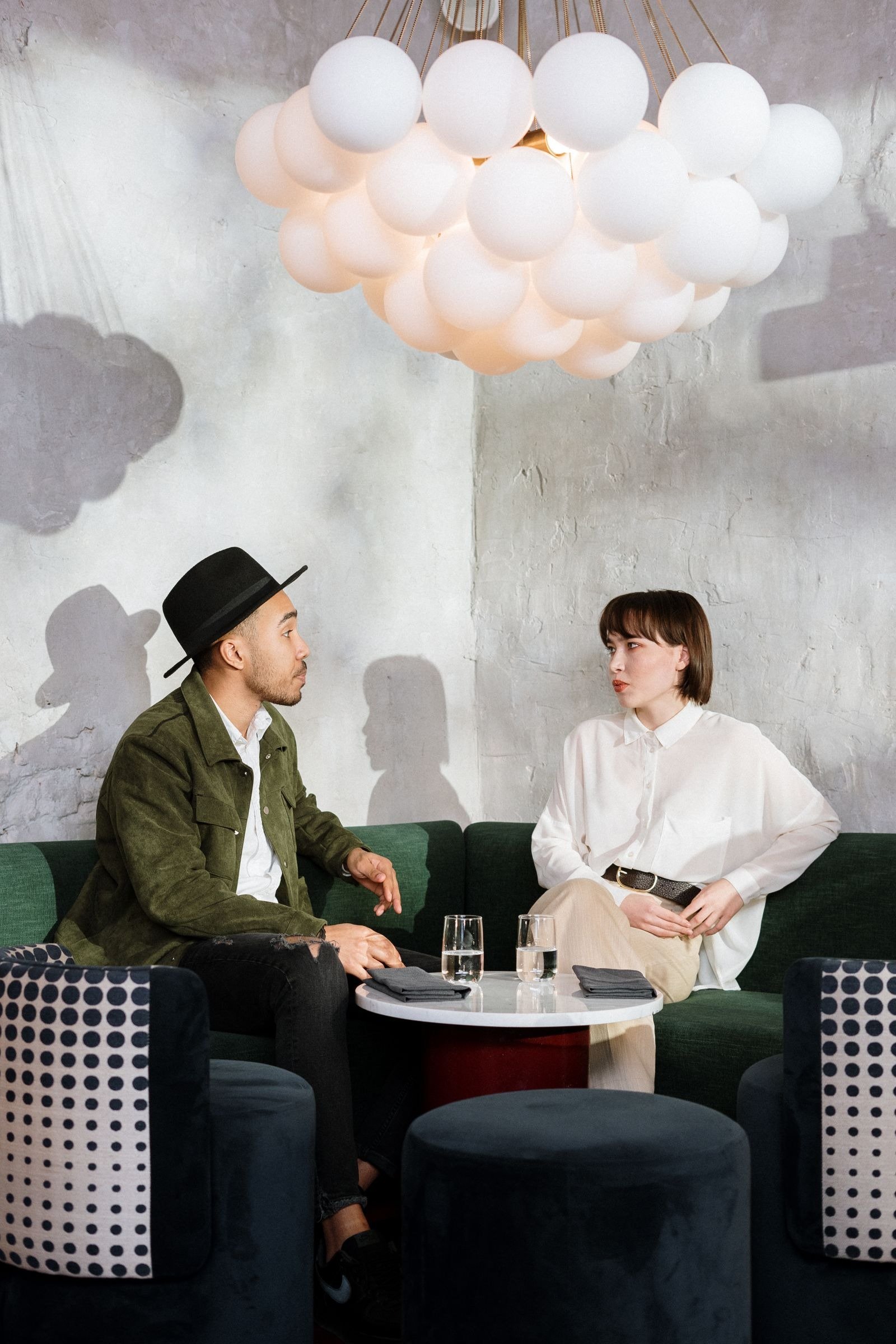 A man and woman talking across a small table in a stylish cafe.