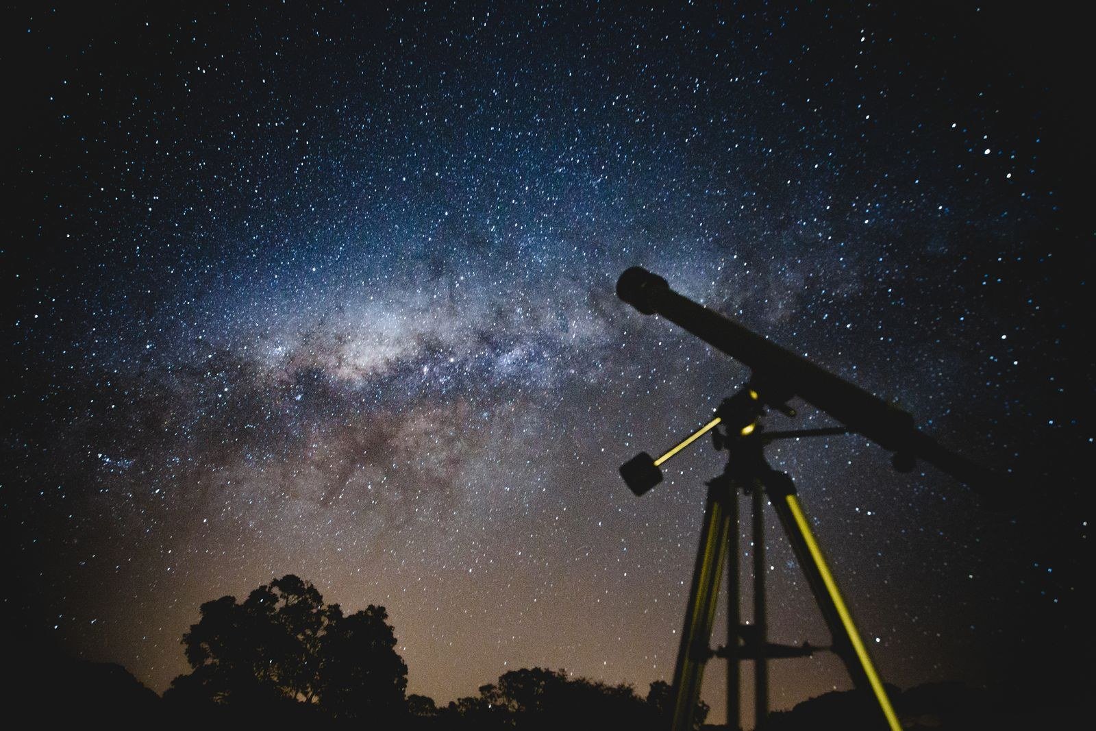 A telescope pointed at the evening sky from a hilltop, silhouetted against deep blue dusk.