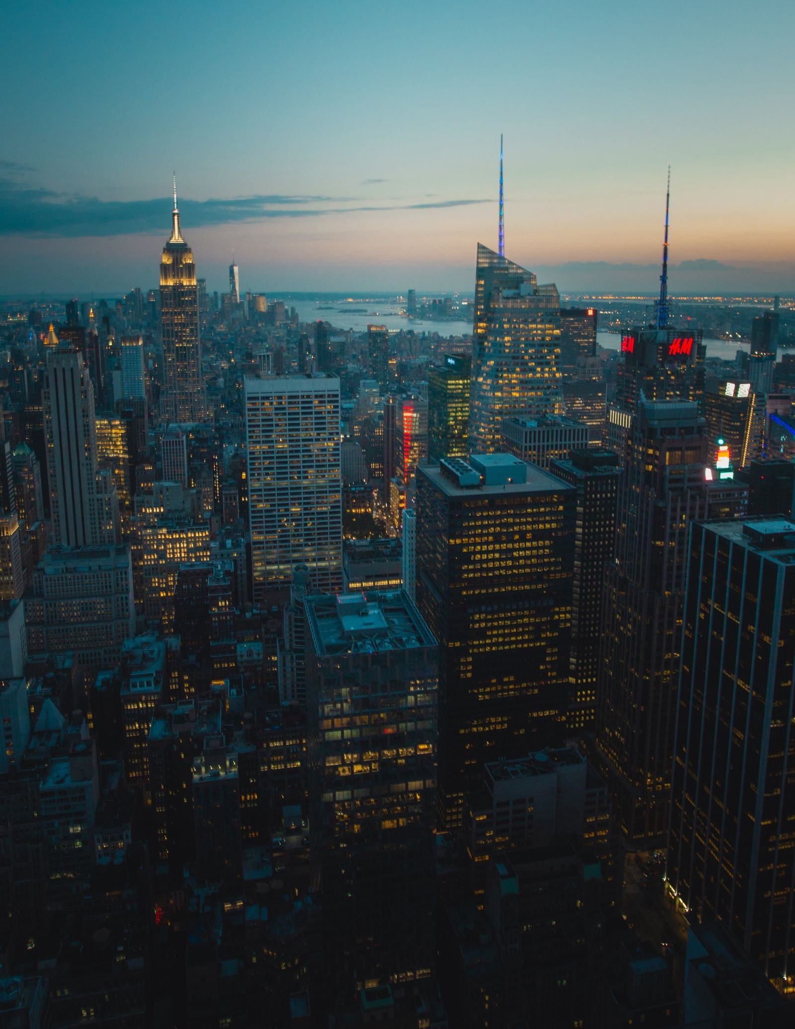 A city skyline at dusk with office windows lit in warm yellow against a purple sky.