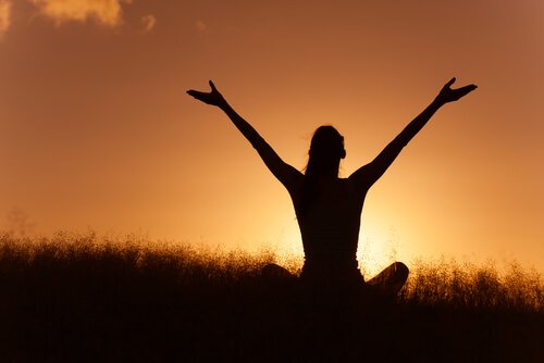 A woman sitting with her arms open at sunset