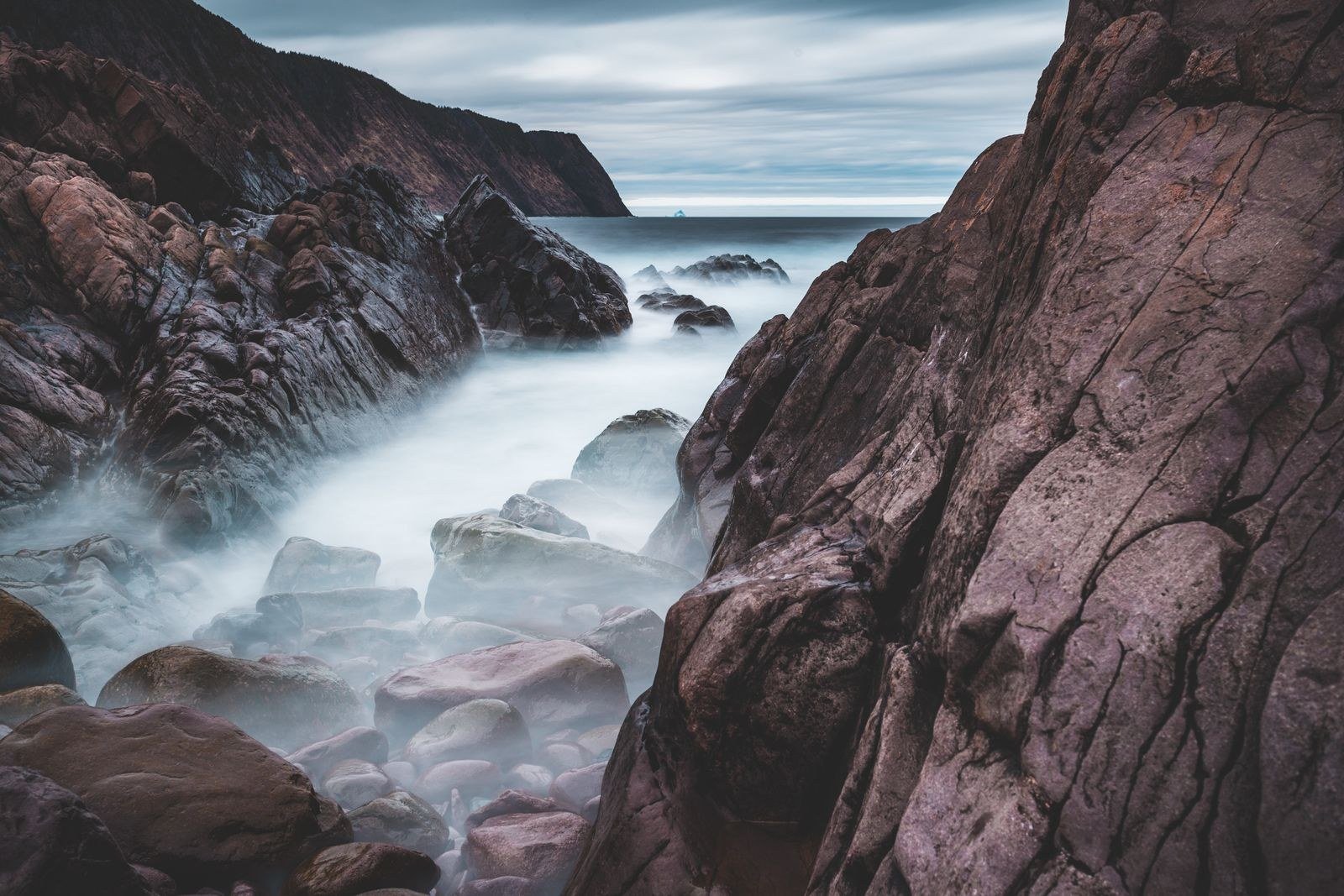 Ocean waves breaking over dark rocks in soft morning mist.