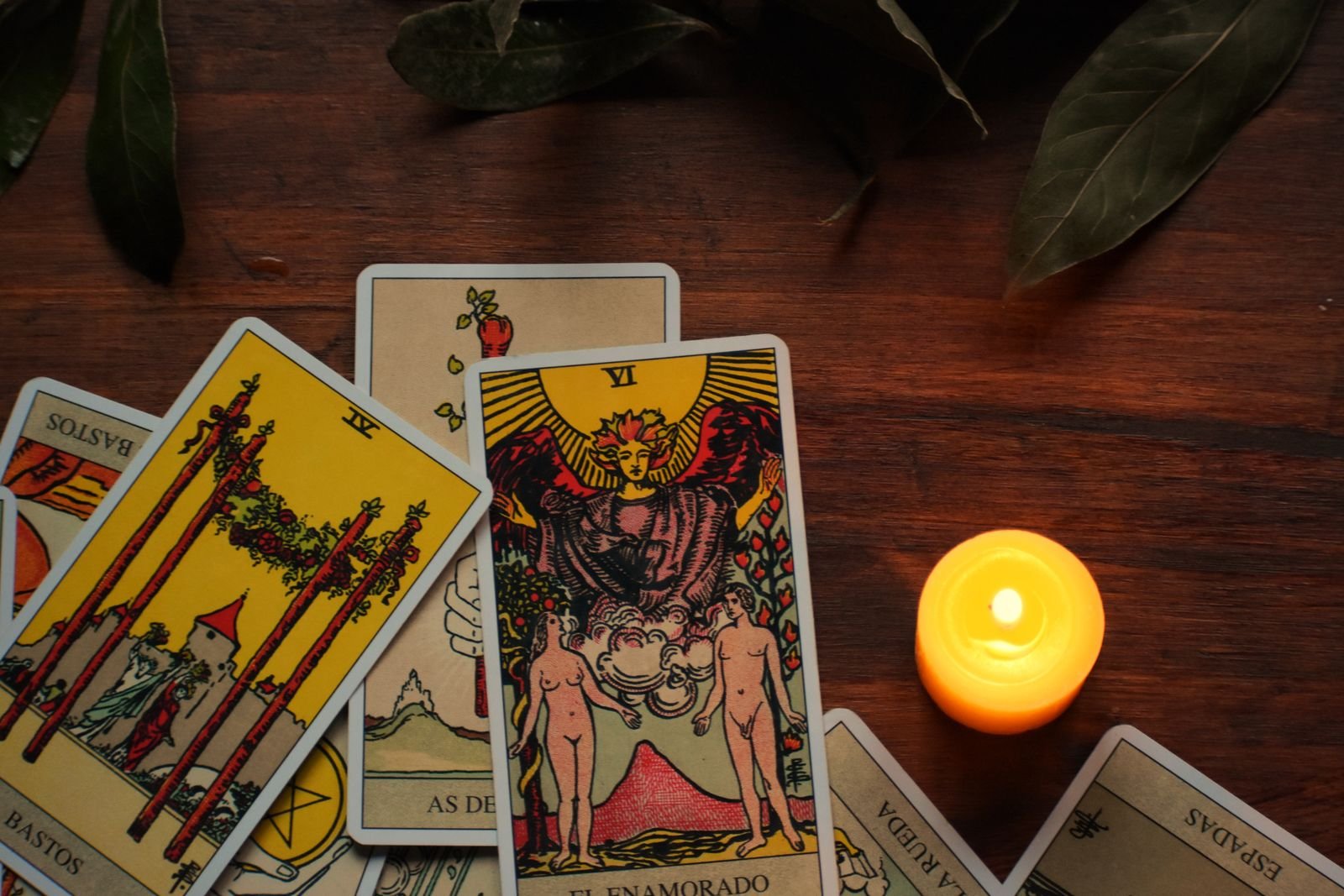 Tarot cards fanned on a wooden table beside a lit tea light candle