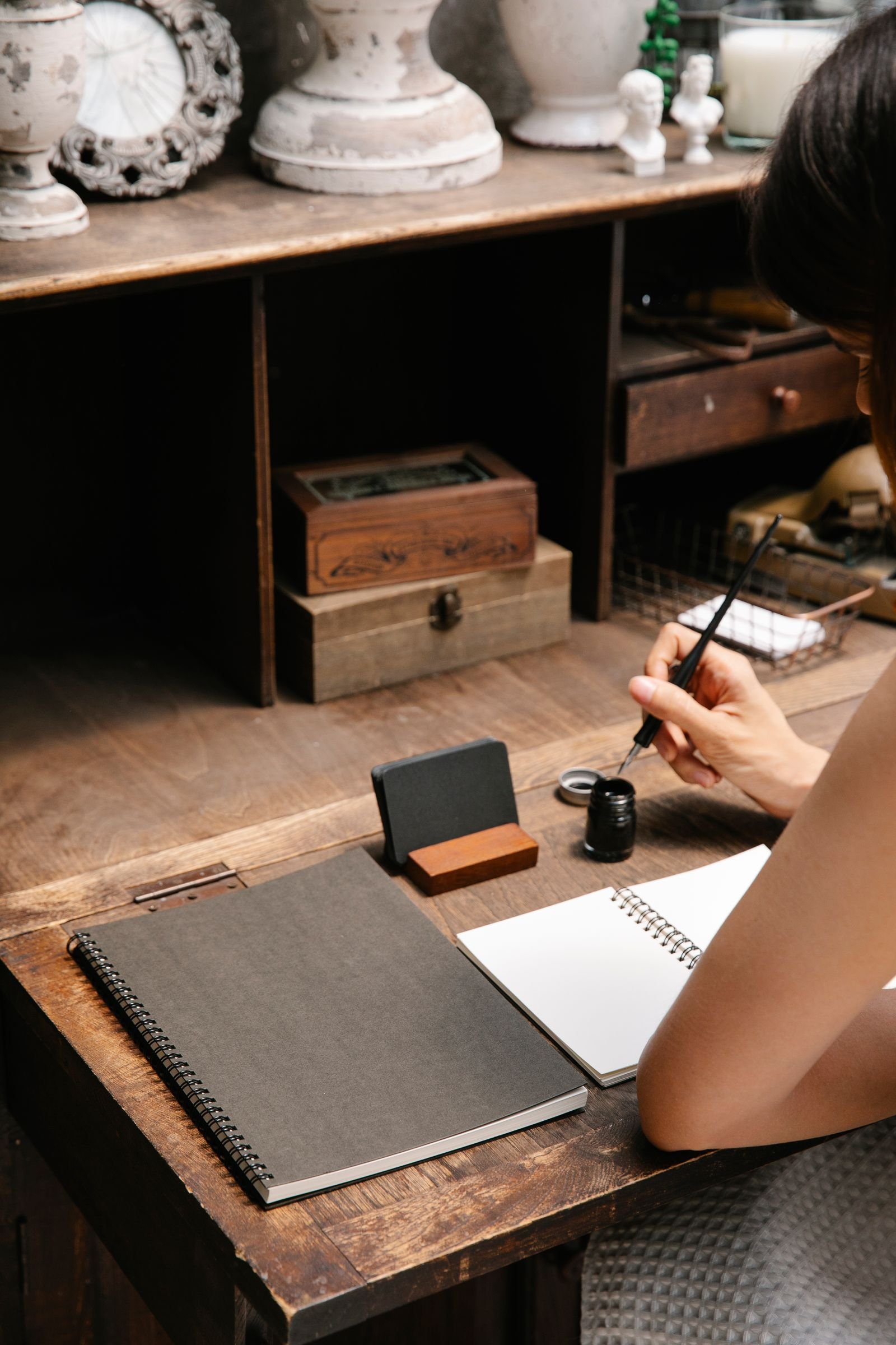 A woman writing with a dip pen in a notebook at a wooden desk