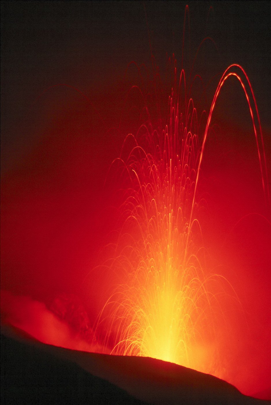 A volcano erupting at night, glowing lava fountaining above dark slopes.