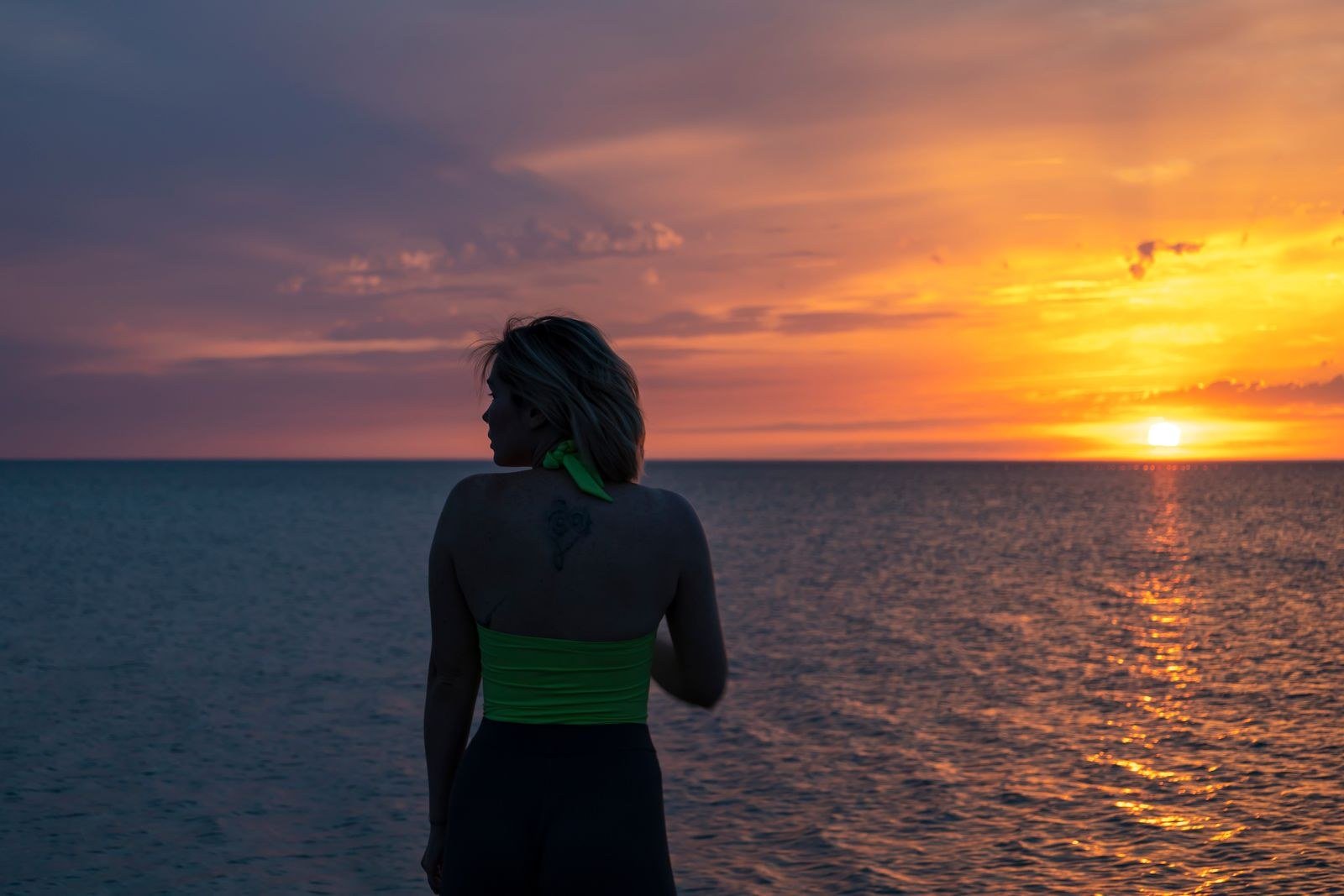 Woman seen from behind watching a colorful sunset over the ocean.