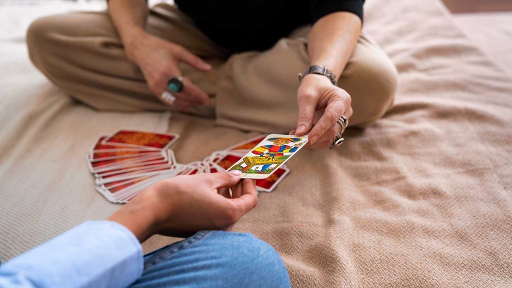 Two people sitting on the floor with tarot cards spread between them, one person handing over a card