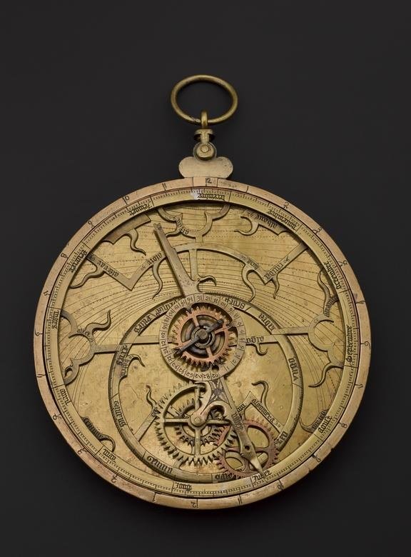 Antique brass astrolabe with engraved dials and gearwork, photographed against a dark background