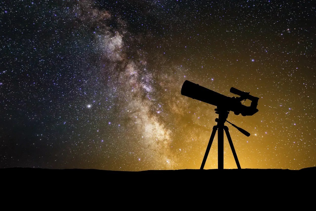 Silhouette of a telescope on a tripod against the Milky Way at dusk