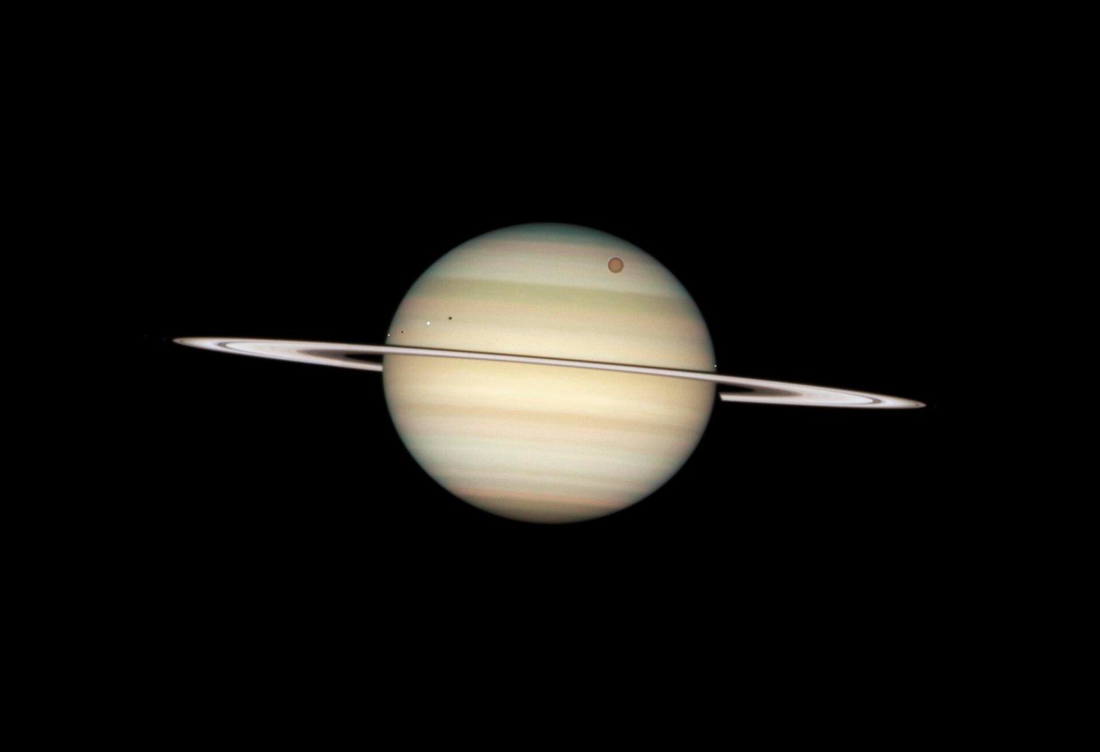 Saturn photographed by the Hubble telescope with the dark shadows of four transiting moons on its cloud tops.