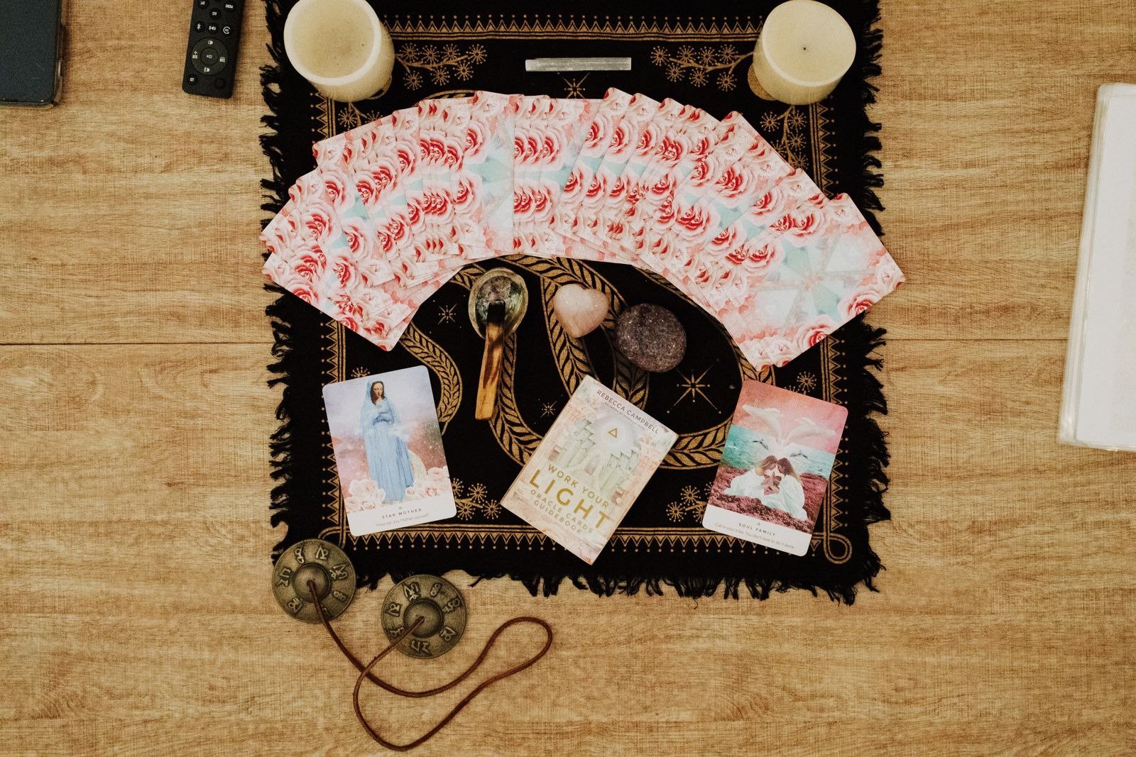 Oracle cards fanned out on a black and gold cloth with candles, crystals, and a guidebook.