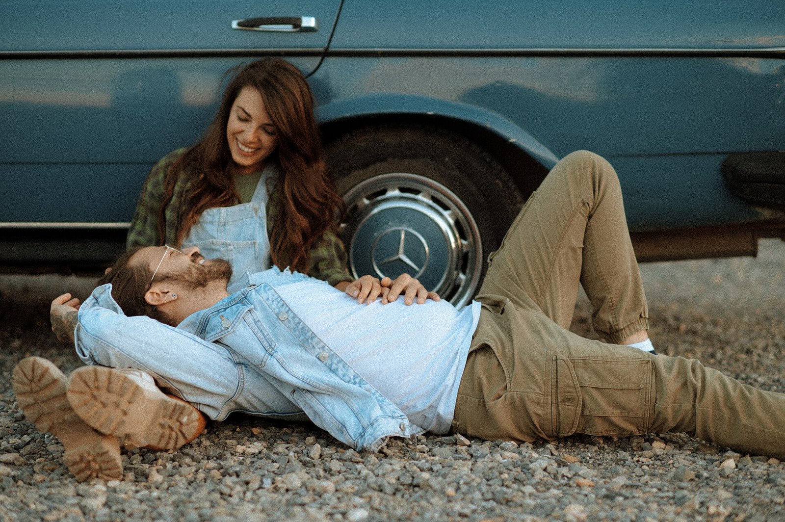A couple relaxing on the ground beside a vintage car