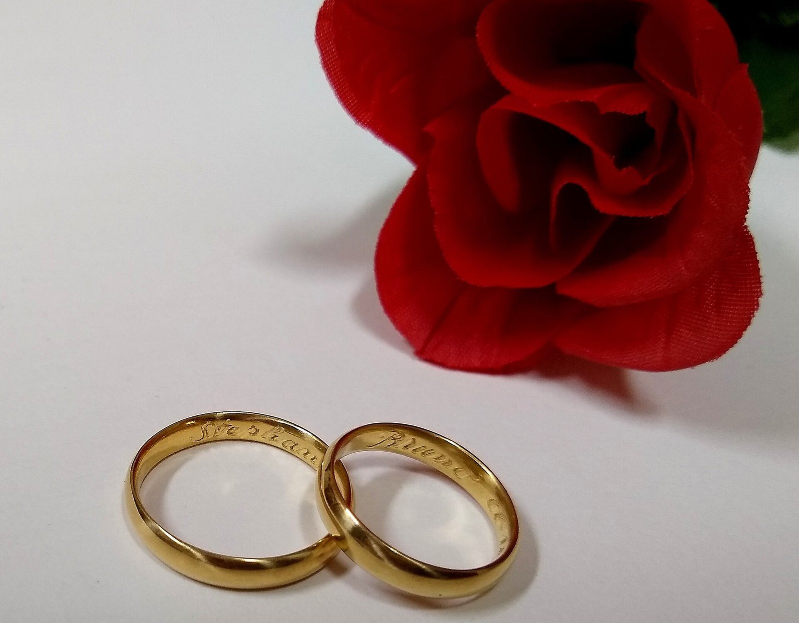 Two gold wedding rings beside a red rose