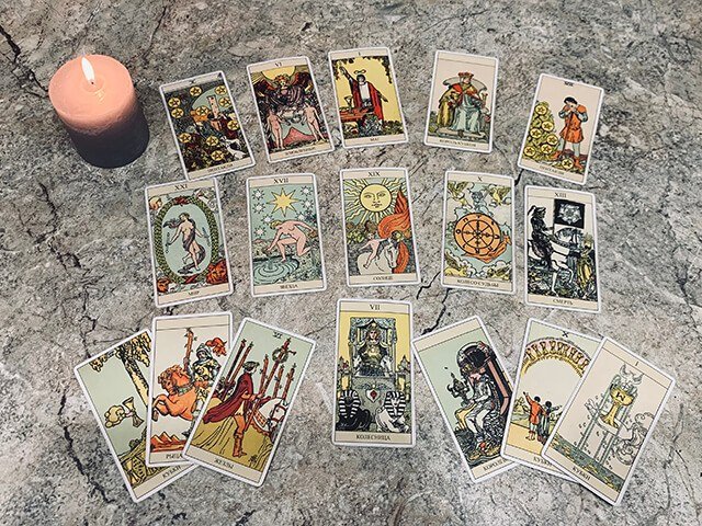 Tarot cards laid face up in rows on a gray marble surface beside a lit candle