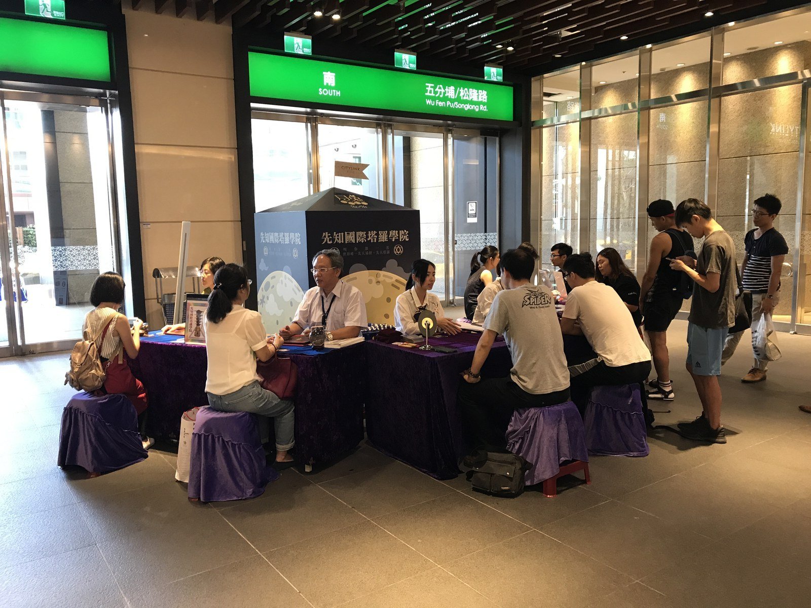 A tarot card reading booth inside a train station, with readers and clients seated at tables covered with purple cloths